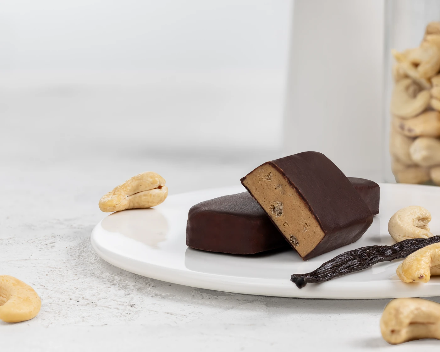 MojoBite vanilla dark chocolate protein bar on plate with vanilla pod and cashews