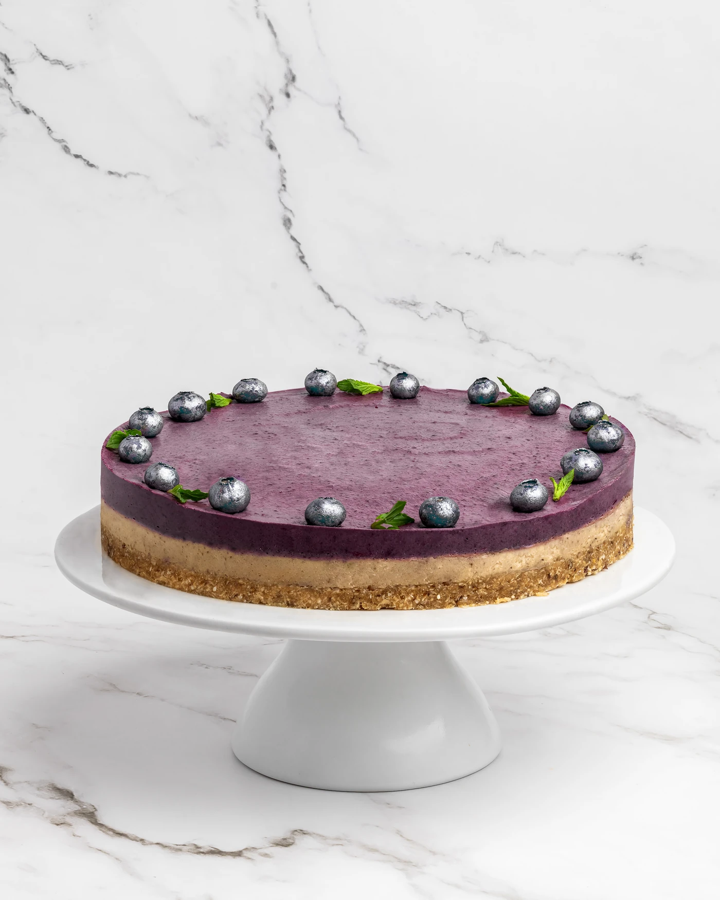 Whole blueberry cake on white pedestal - vibrant purple with fresh blueberry garnish ring