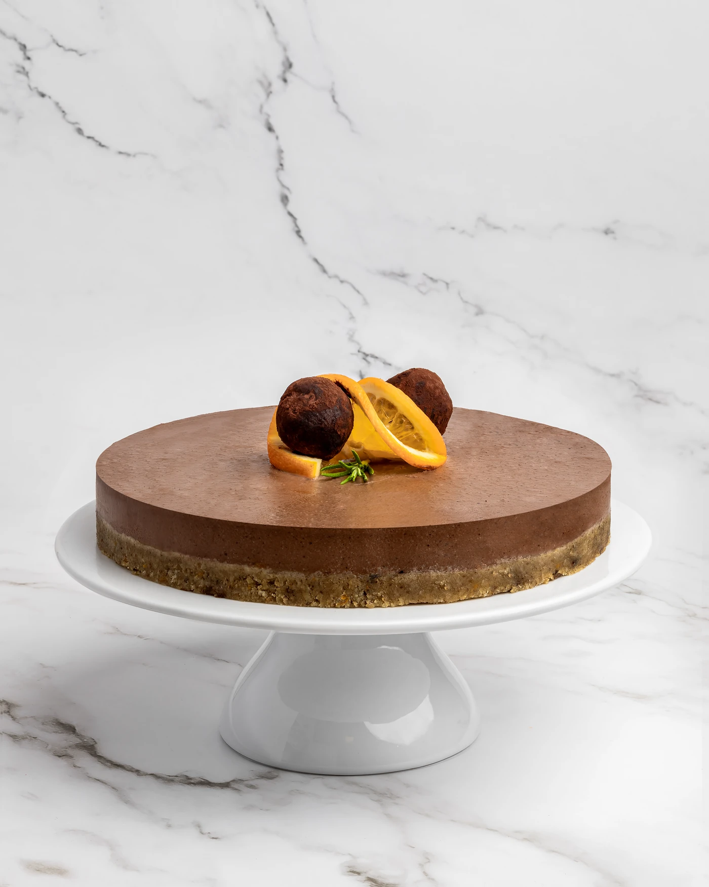 Whole chocolate orange cake on pedestal with truffle and orange garnish - rich dark layers