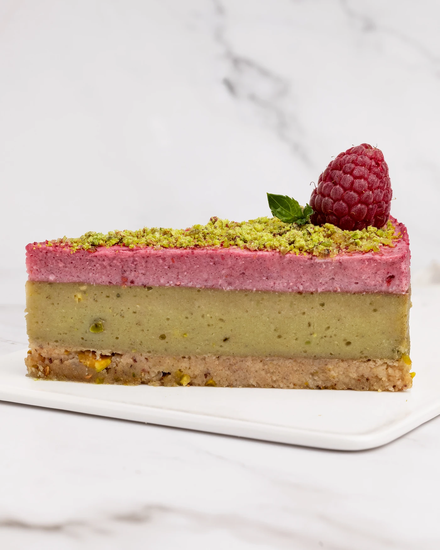 Raspberry pistachio slice - four vibrant layers with fresh raspberry garnish