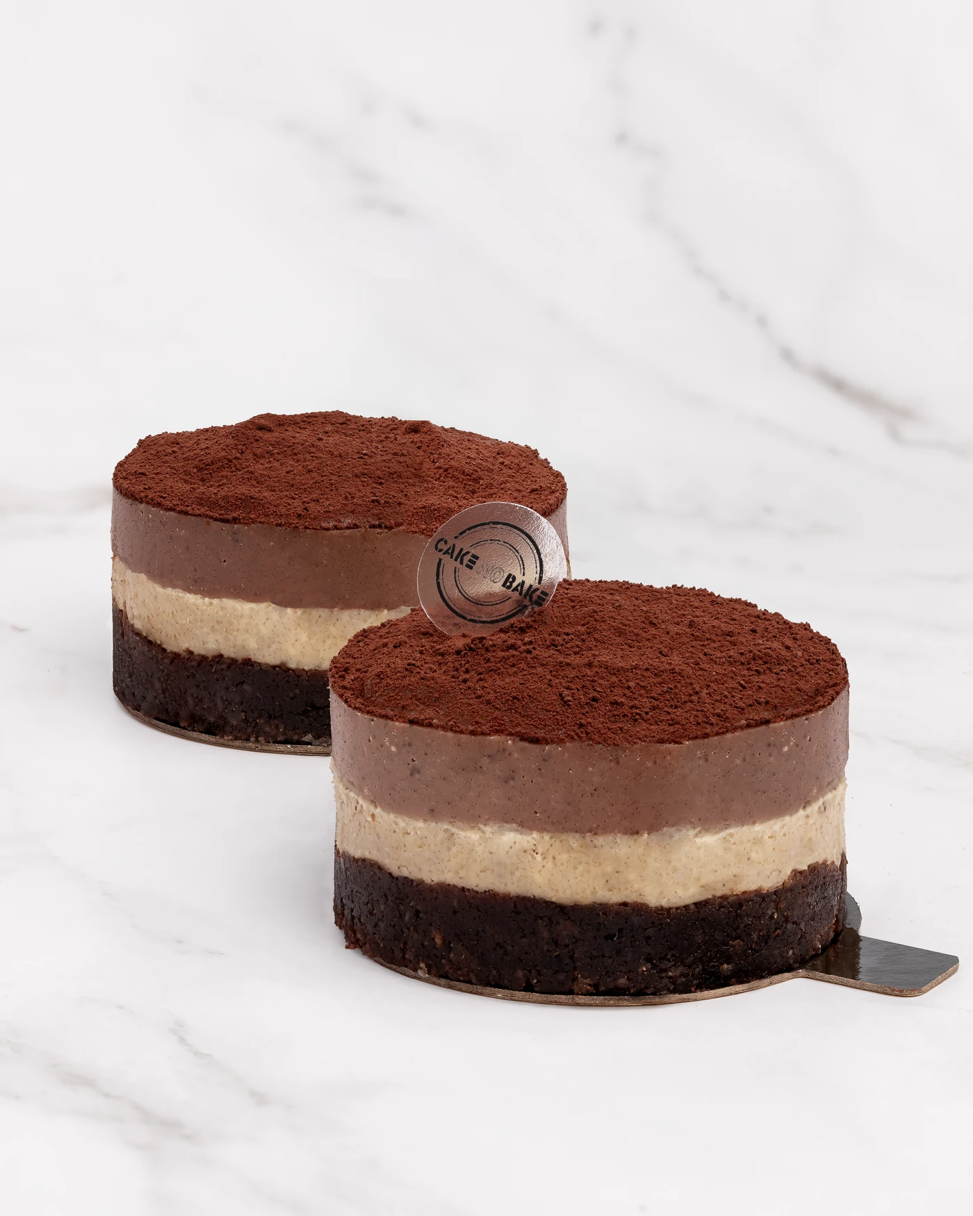 Tiramisu-style raw vegan cake with cocoa dusting and brand stamp