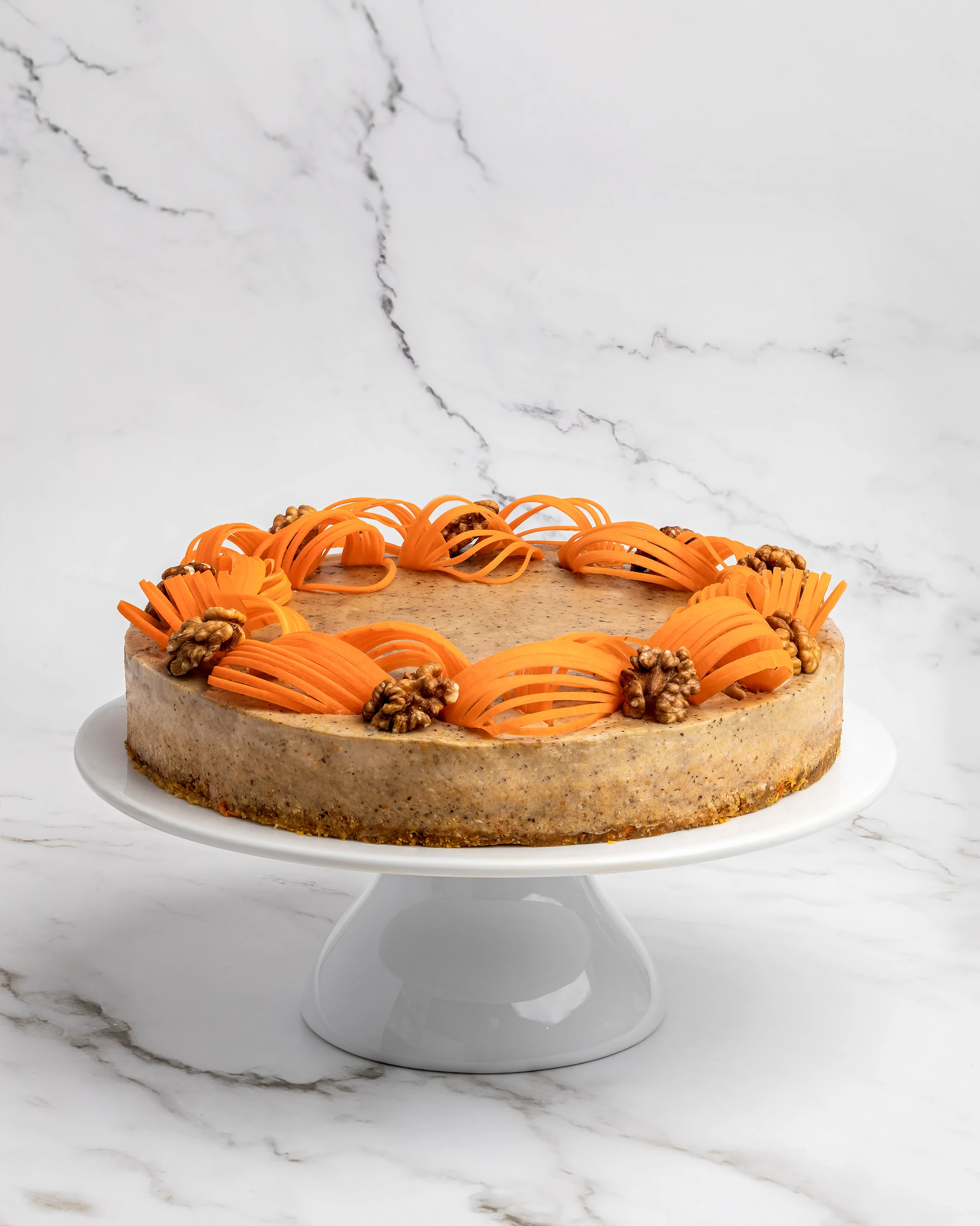 Cake No Bake orange walnut raw vegan cake on white pedestal - decorative orange curl ribbon and walnut garnish ring on marble