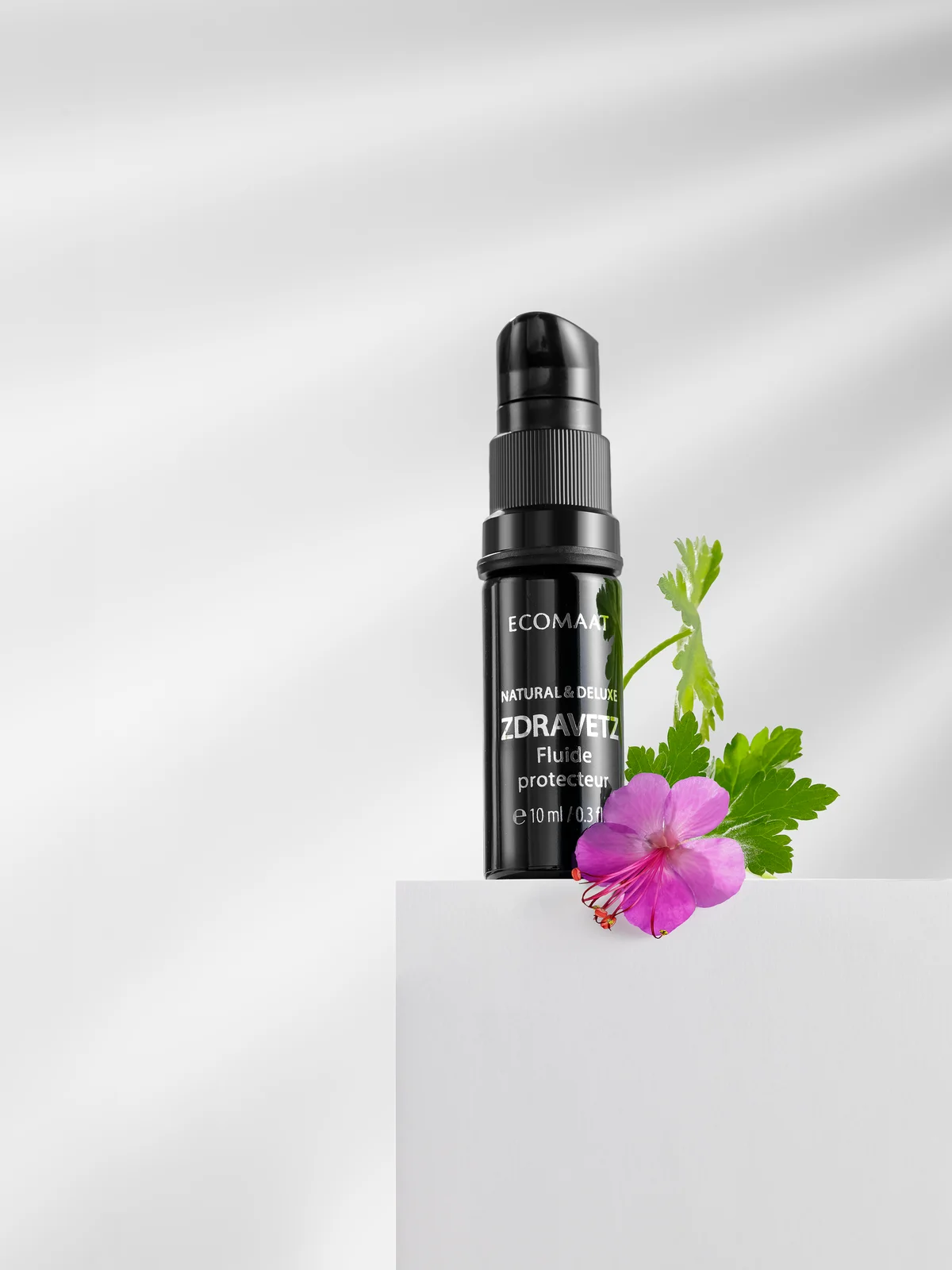 ECOMAAT black bottle on pedestal with fresh pink flower accent