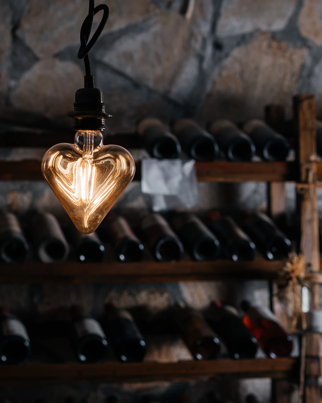 Сърцевидна ретро крушка в рустикална каменна изба на Вила Винифера с бутилки българско вино.