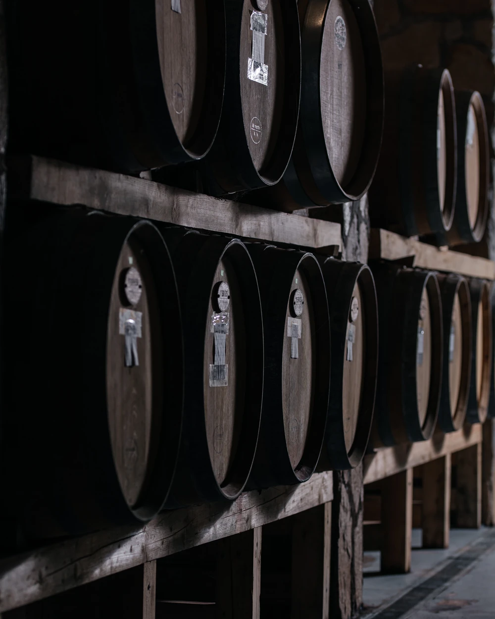 Рустикални винени бъчви, подредени на стелажи в тъмната изба на Villa Vinifera, Пловдив, България.