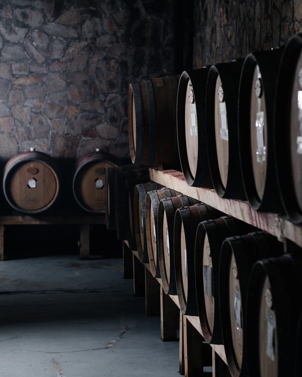 Винени бъчви, подредени на стелажи, в каменна изба на Вила Винифера, дом на изискани български вина до Пловдив.