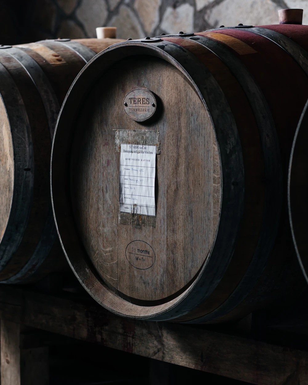 Дървени бъчви на винарна Villa Vinifera в каменна изба, една с плакет TERES и 36 месеца, отлежаващи българско вино.