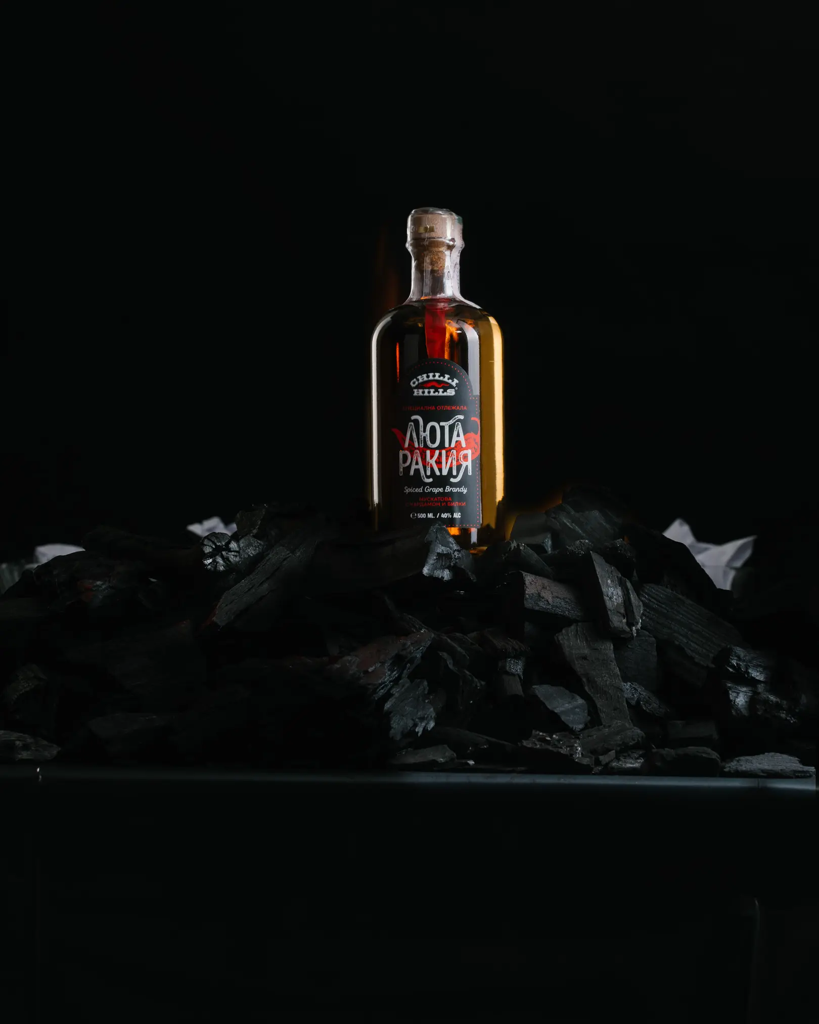 Бутилка подправена гроздова ракия Chilli Hills върху горящи въглени за майсторски клас по продуктова фотография Dynaphos.