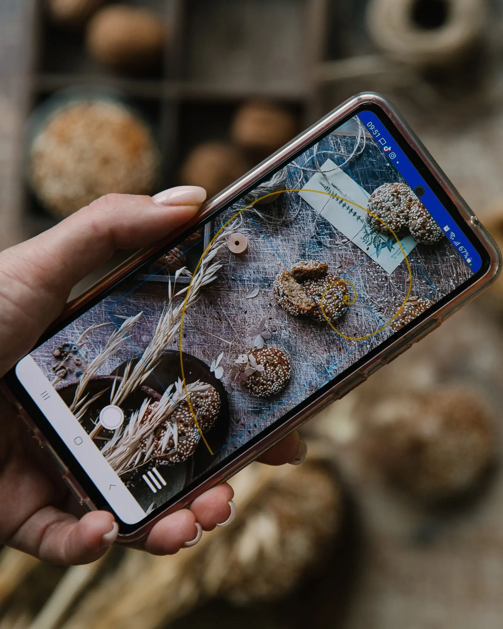 Смартфон демонстрира фуд фотография с триъгълна композиция на стилизирани бисквити със семена и реквизит.