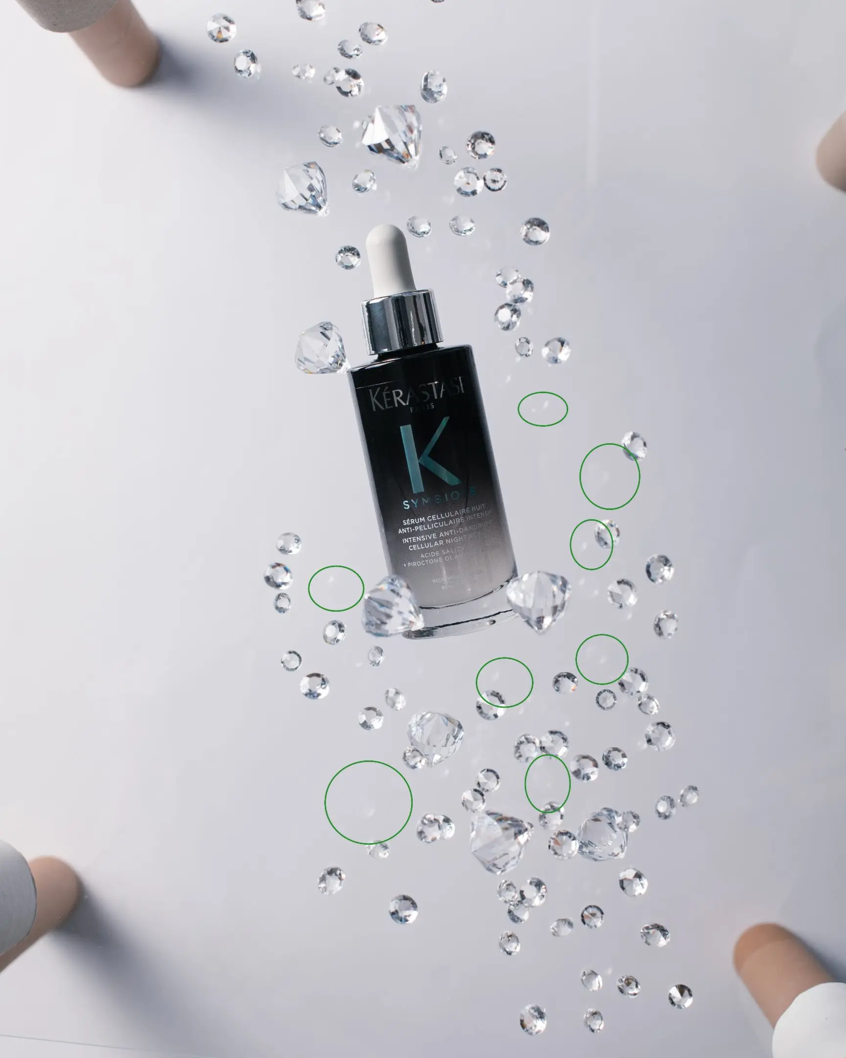 Kérastase Symbiose serum bottle floating with crystalline droplets on white, demonstrating glass product photography.