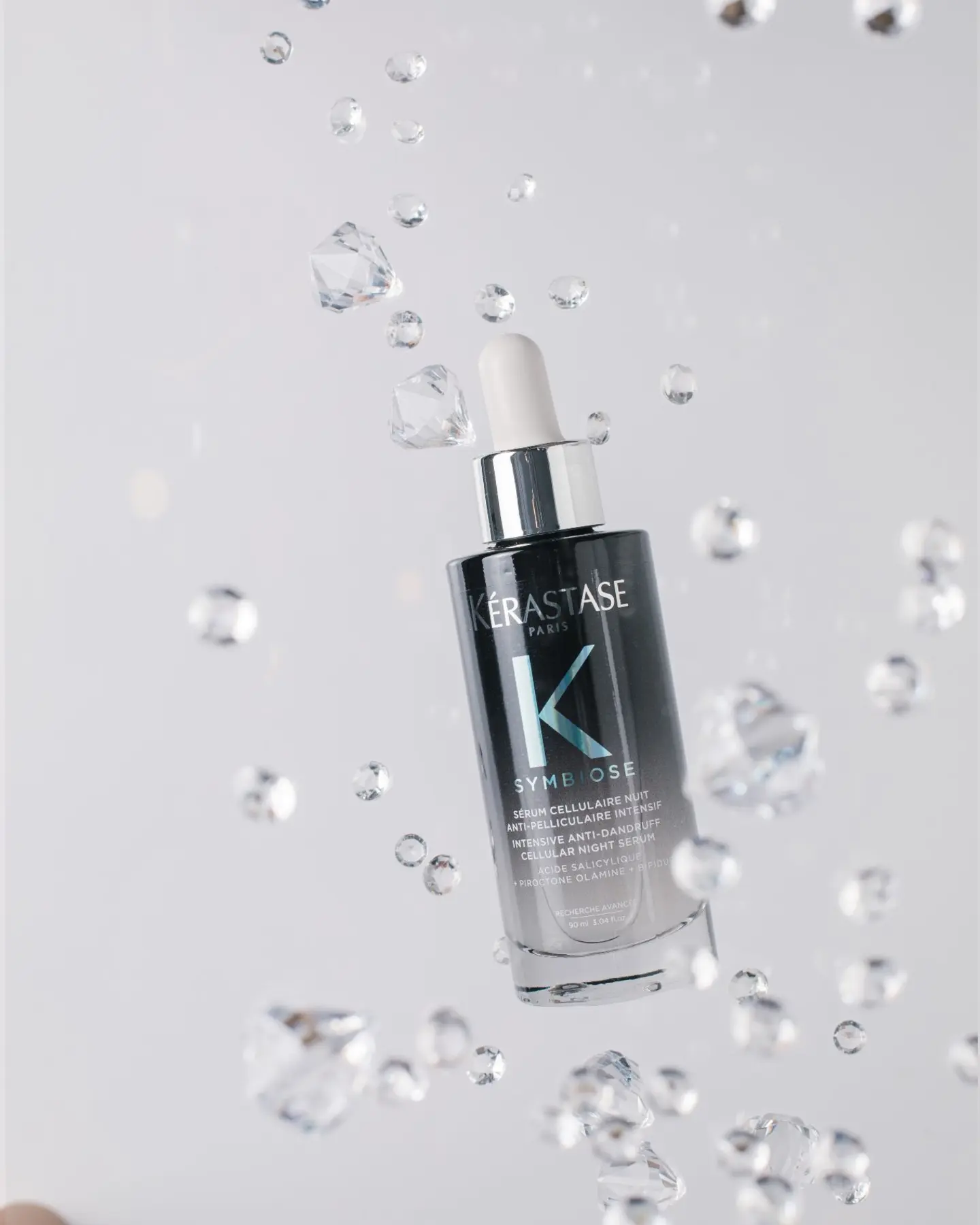 Kérastase Symbiose Cellular Night Serum bottle among suspended droplets, highlighting the wow effect for product photography.