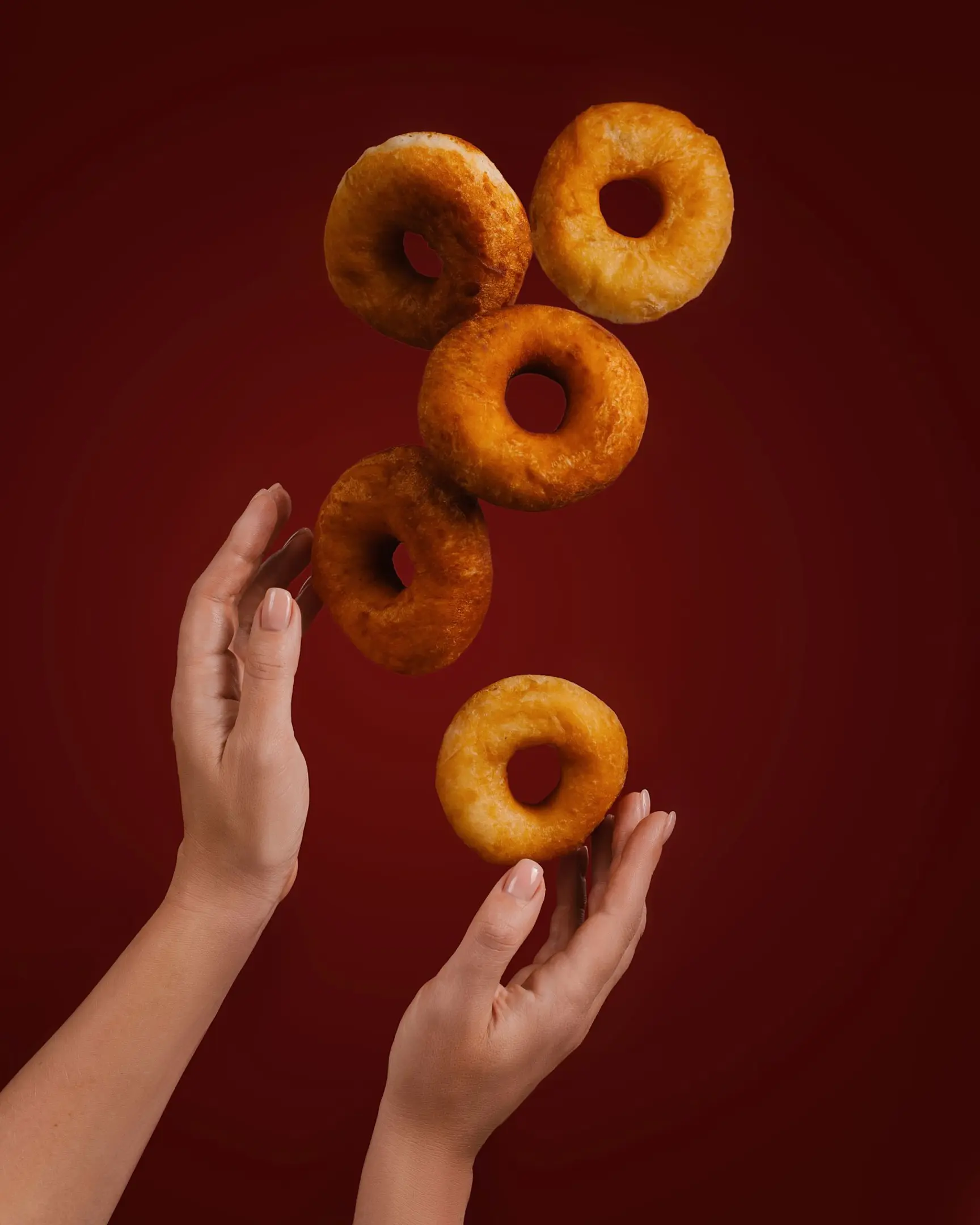 Golden donuts floating above hands on red, demonstrating a "wow effect" for product photography using glass.
