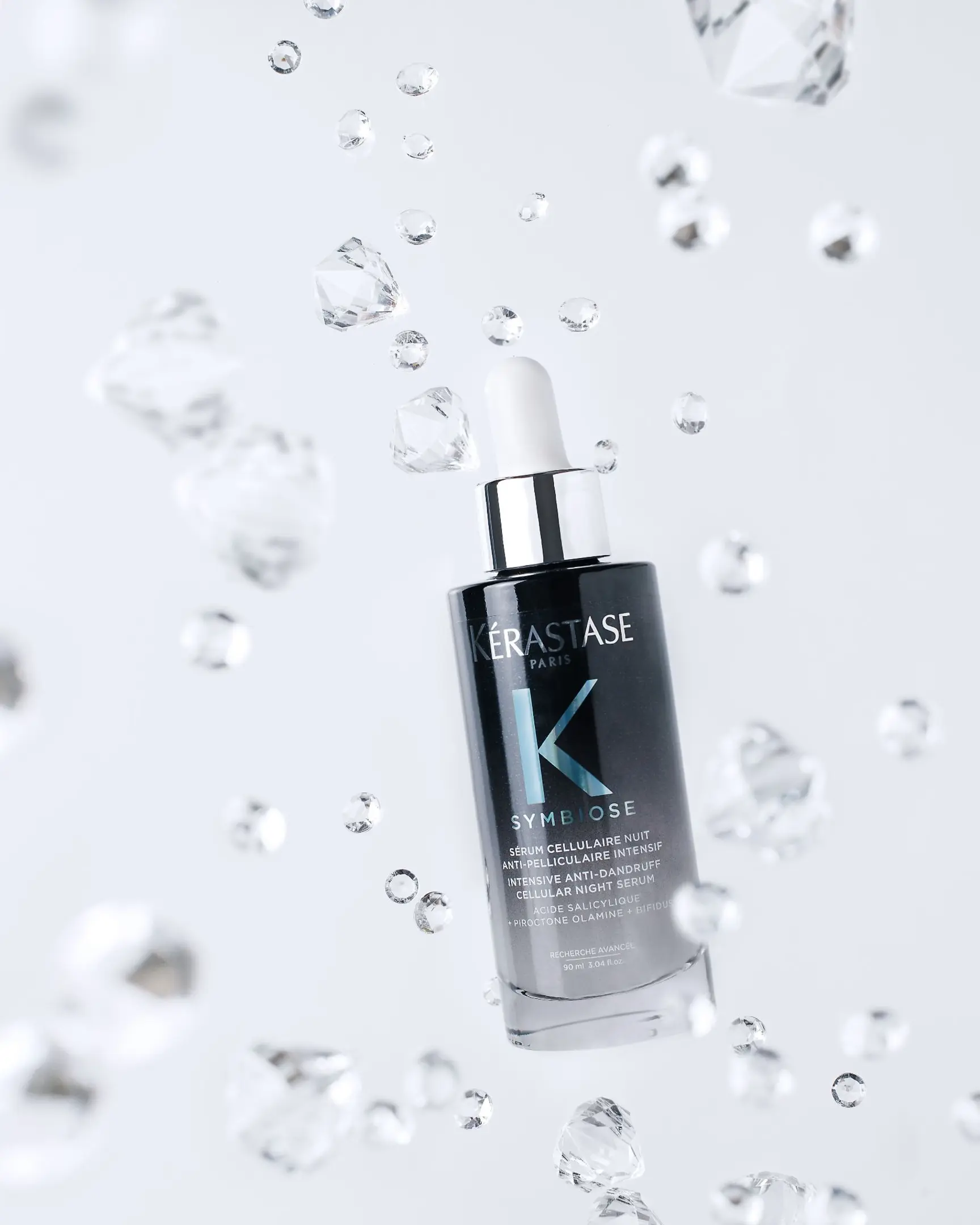 Kérastase Symbiose Anti-Dandruff Night Serum bottle with floating crystals & droplets for product photography.