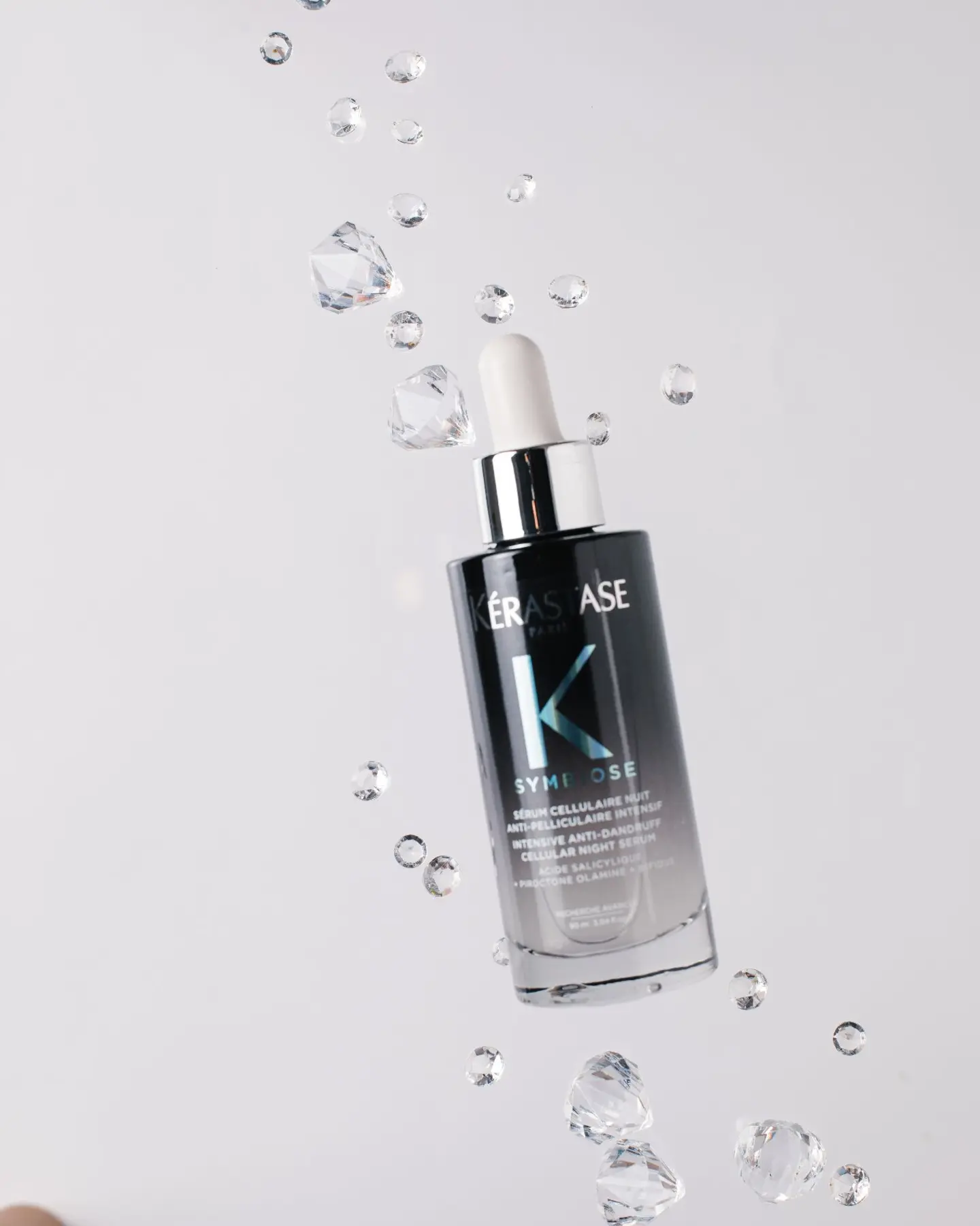 Kérastase Symbiose Night Serum floating with crystals on white, showing suspended droplets effect for product photography.