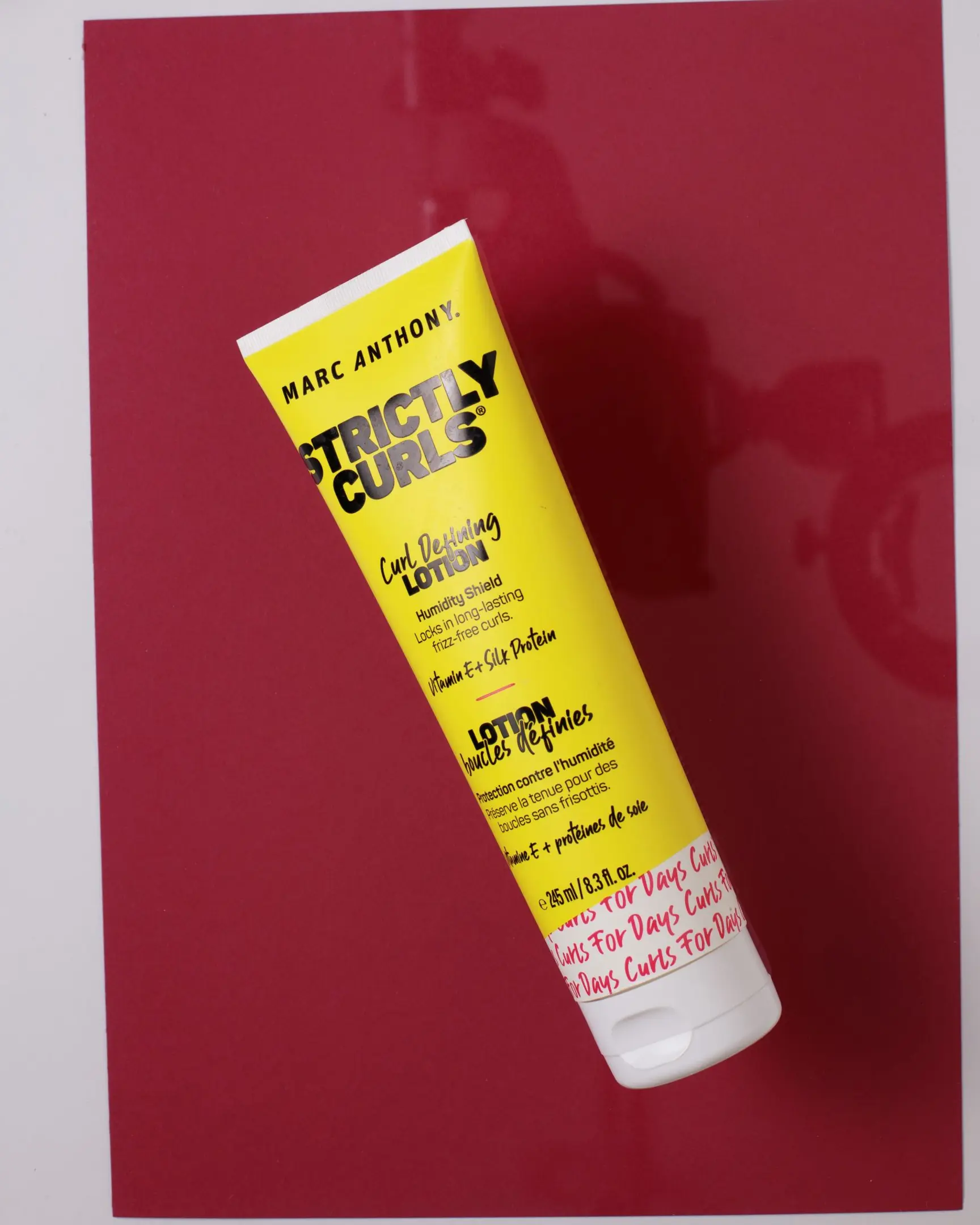Marc Anthony Strictly Curls Curl Defining Lotion yellow tube on red, for product photography with glass.