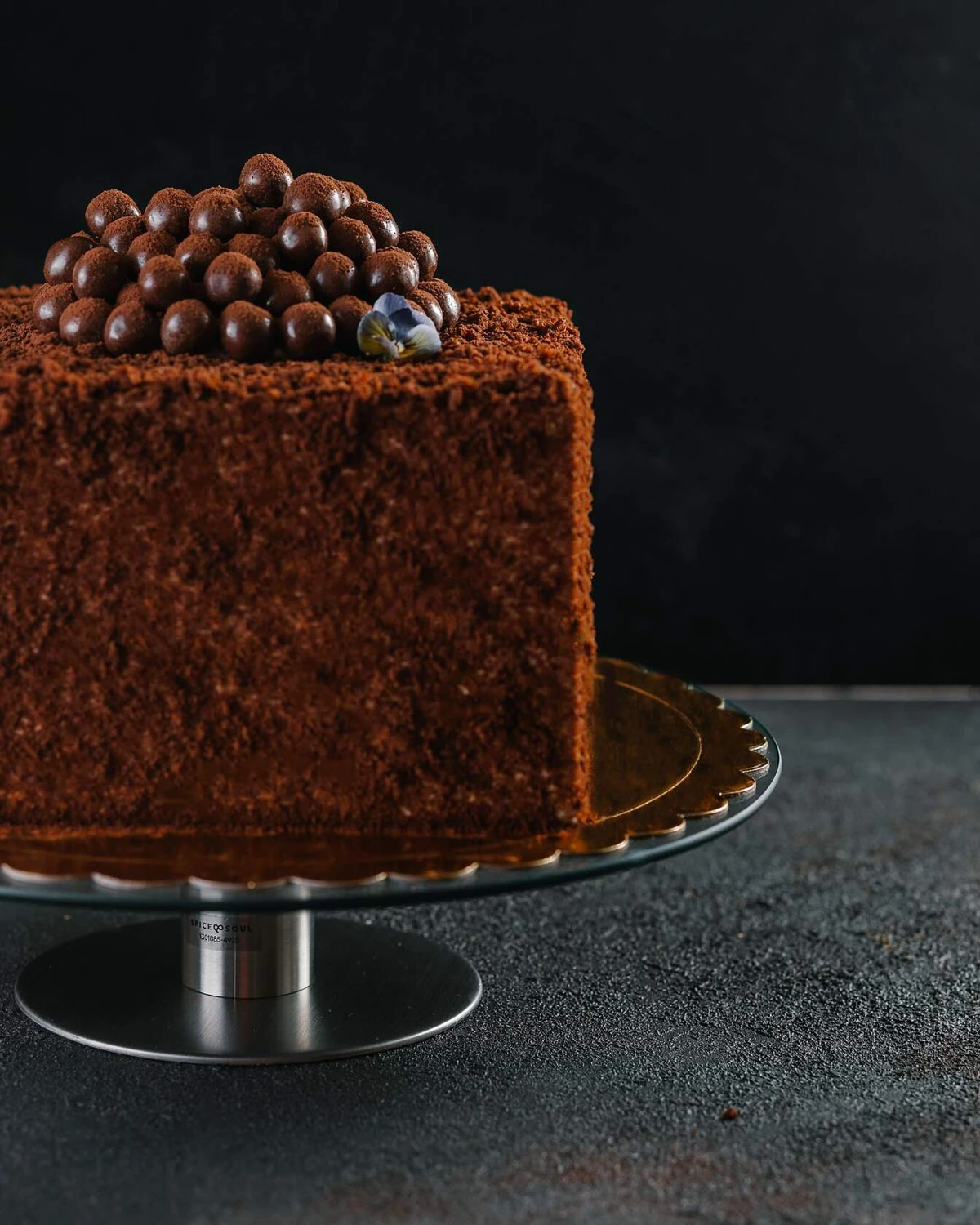 Chocolate Honey cake with caramel milk cream, topped with crispy balls & flower on SPICE & SOUL stand.