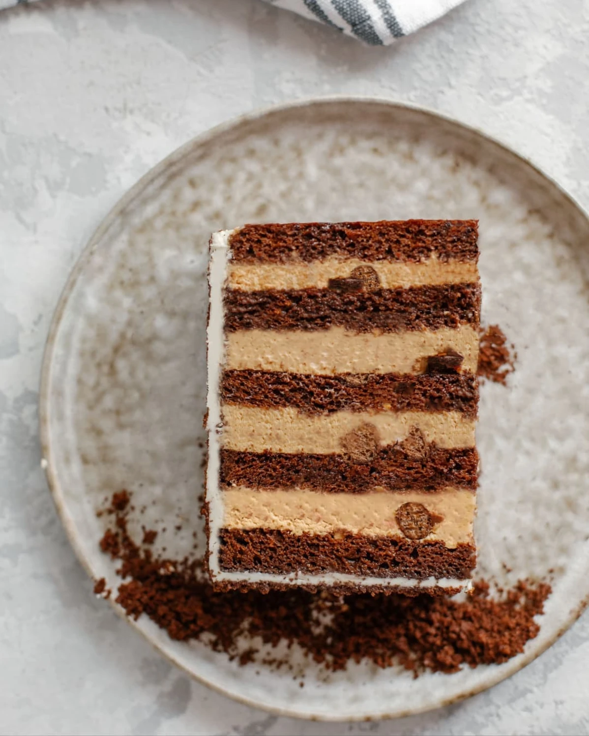 Slice of layered honey cake with chocolate layers, caramel milk cream, and crispy balls on a plate.