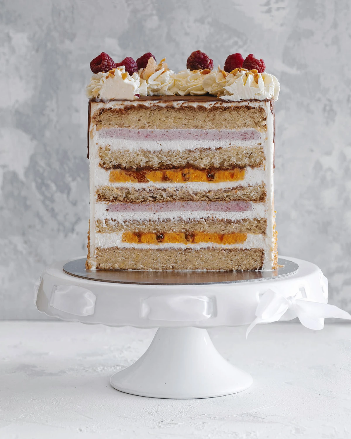 Sea buckthorn cake showing its sponge, strawberry mousse, and vibrant orange sea buckthorn cream layers, topped with raspberries.