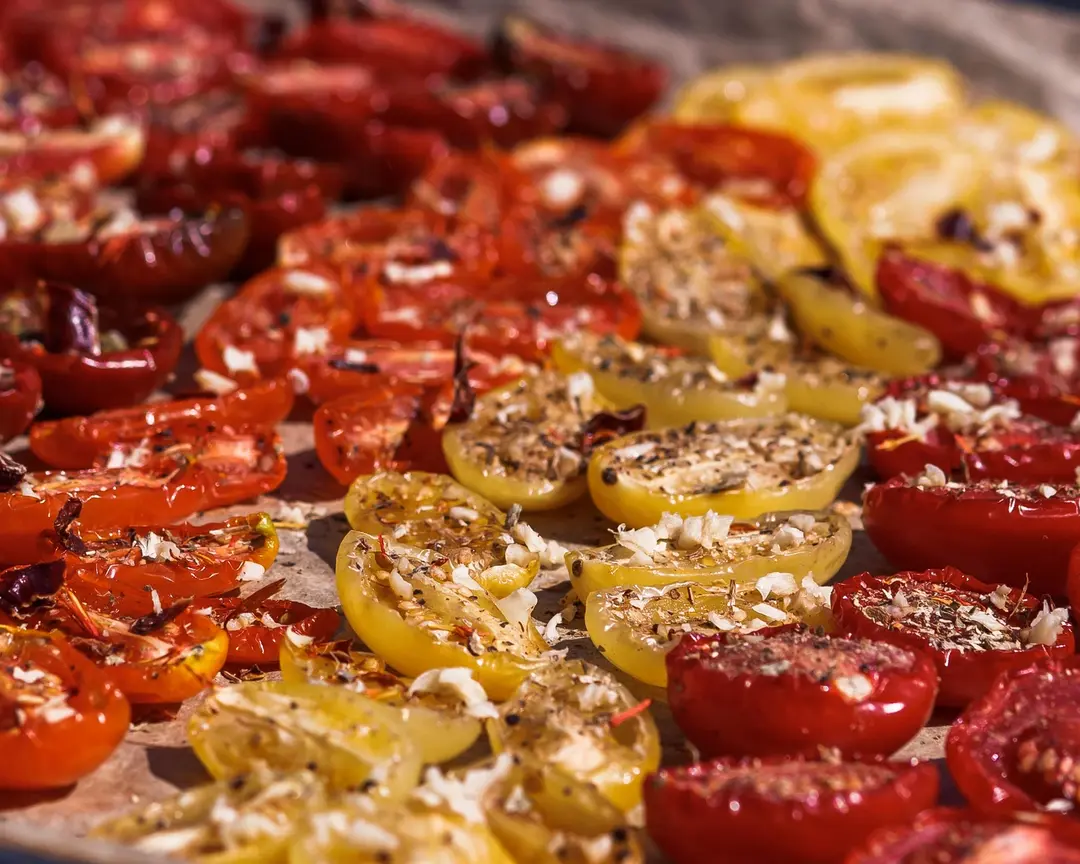 Halved red & yellow cherry tomatoes seasoned with garlic & Provencal herbs on a baking sheet for sun-drying.
