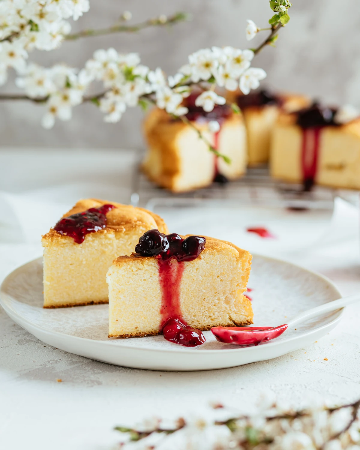 Delicious Russian cottage cheese pie slices with homemade cherry berry sauce & cherry blossoms.