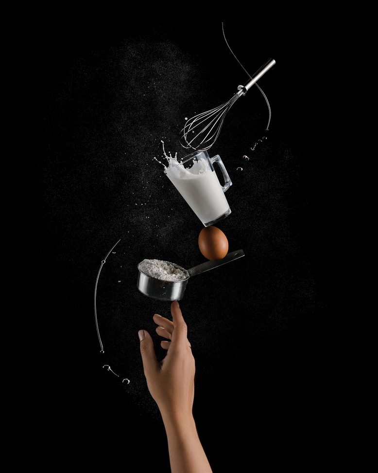 Летящи съставки за палачинки: брашно, яйце, пръскащо мляко, бъркалка. Динамична снимка за лесна рецепта.