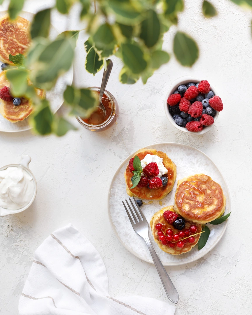 Lush fluffy pancakes with fresh raspberries, blueberries, red currants, cream, and honey drizzle.