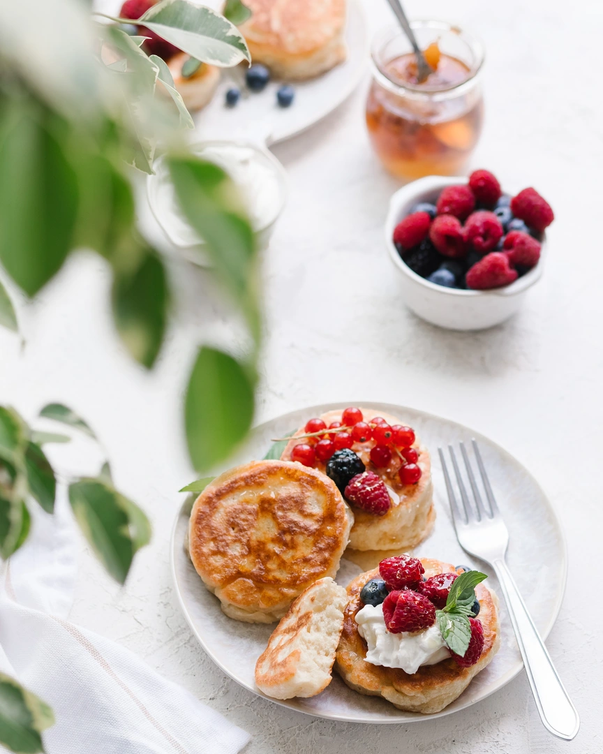 Golden fluffy kefir pancakes with fresh berries, whipped cream, and honey, showcasing their airy texture.