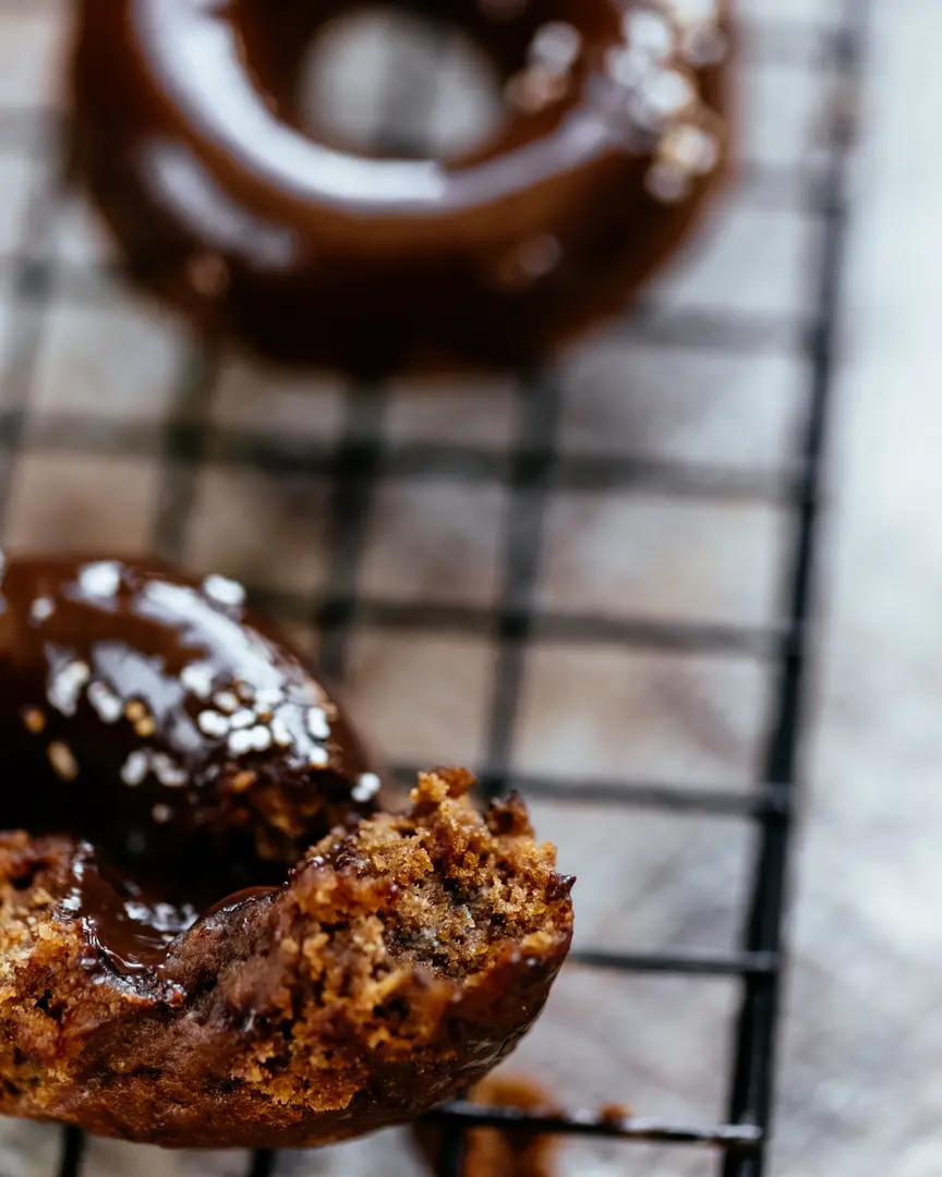 Прясно изпечен тиквен мъфин, разчупен, показващ шоколадови капки и кръмбъл, с друг мъфин на заден план.