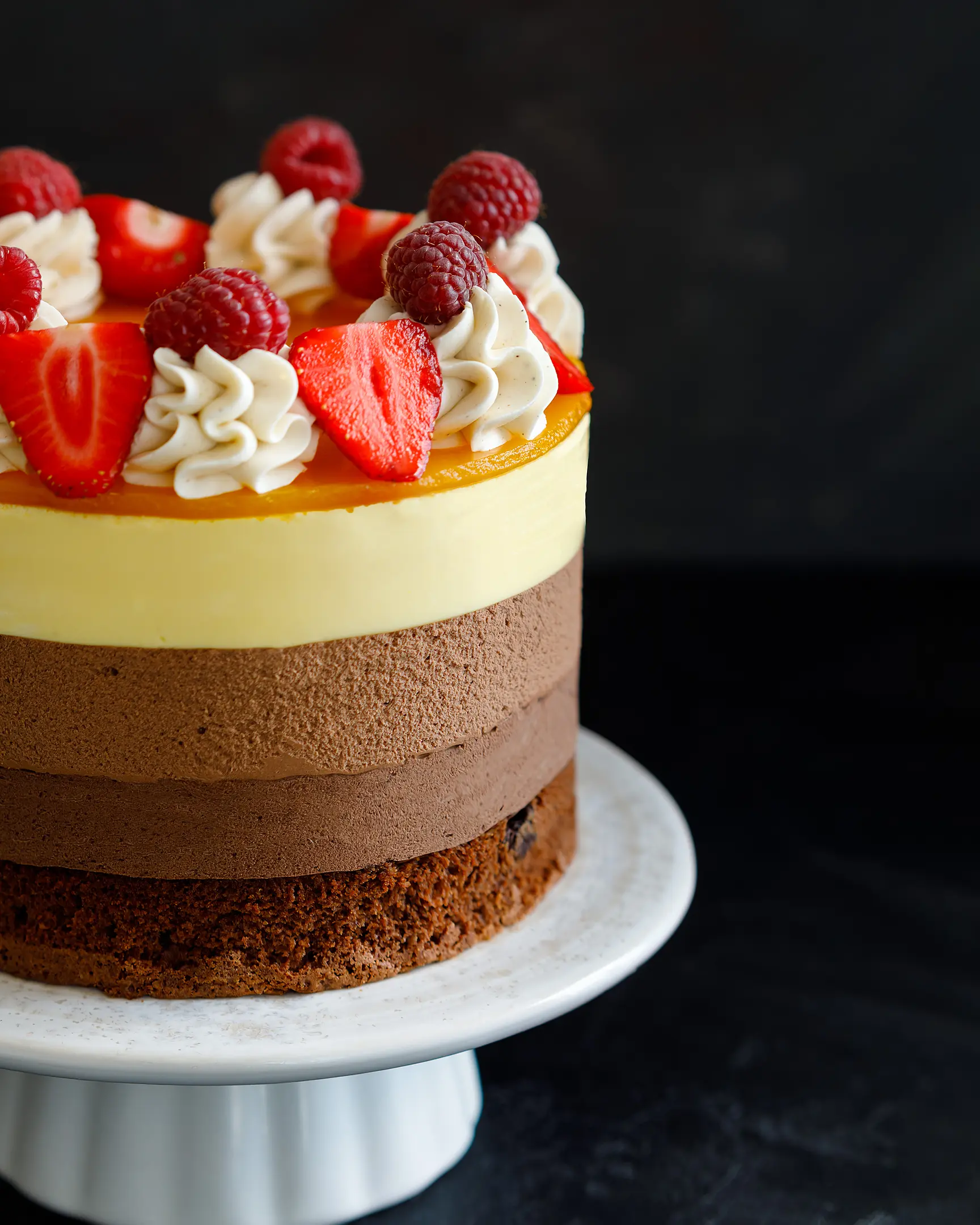 Triple Chocolate Mousse Cake with mango, brownie base, mango jelly, topped with fresh raspberries and strawberries.