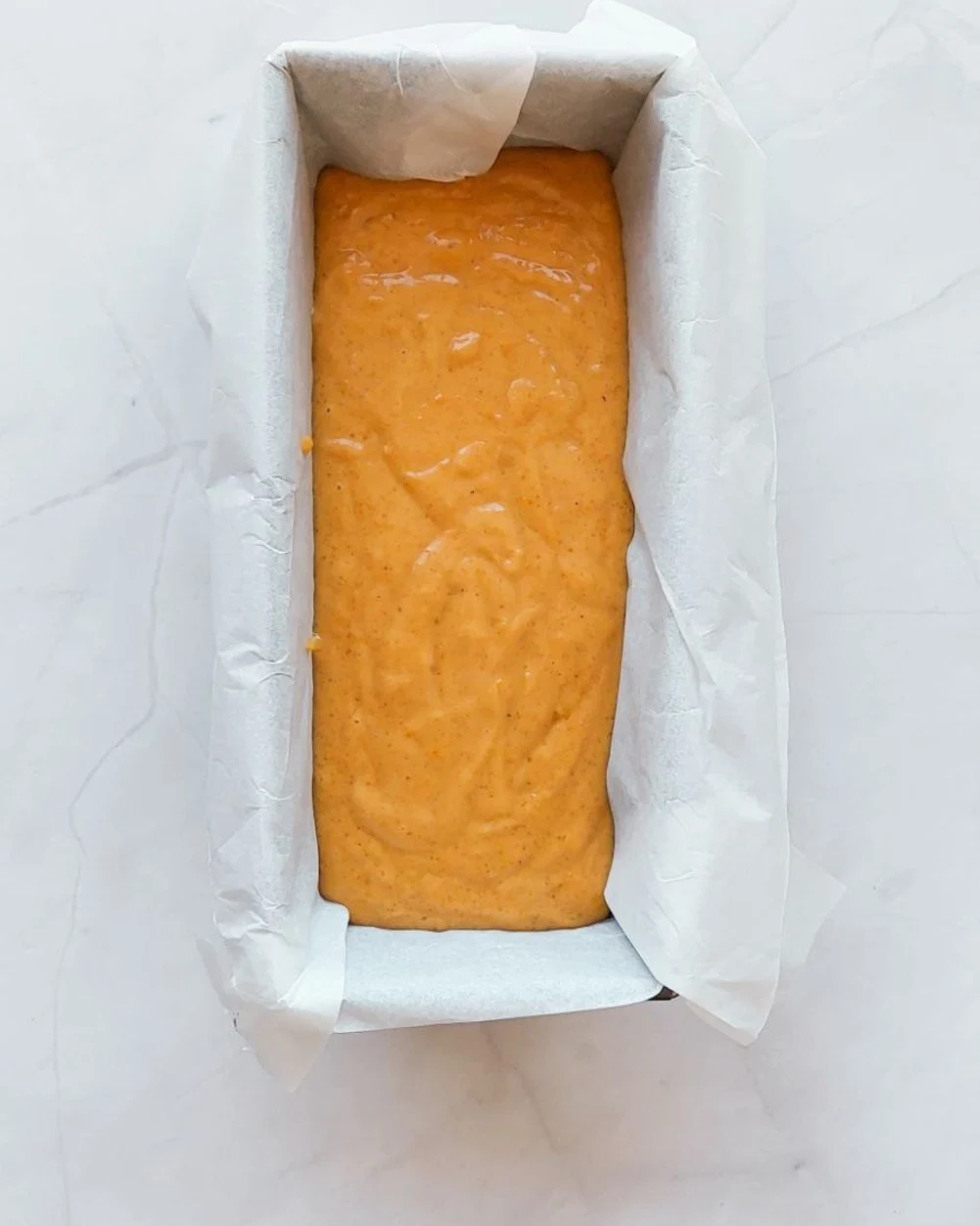 Pumpkin bread batter fills a parchment-lined loaf pan, ready for baking.