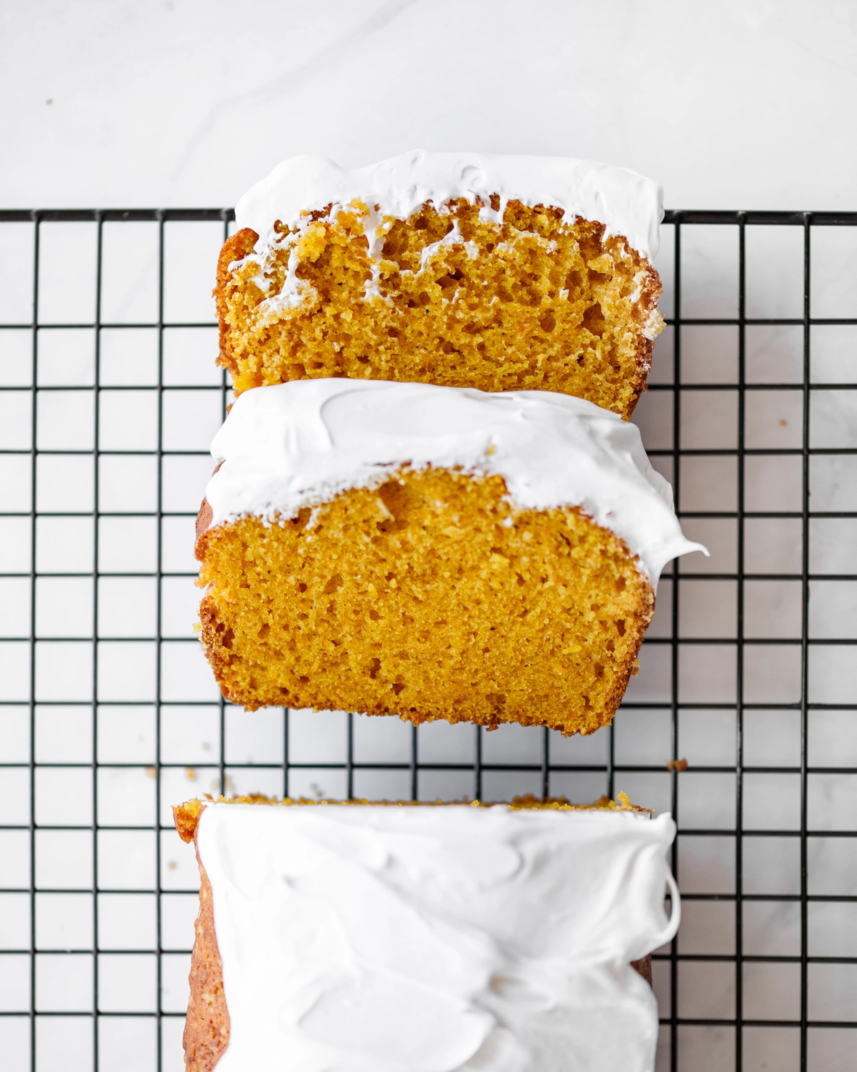 Three slices of pumpkin bread topped with mascarpone or egg white cream, cooling on a wire rack.