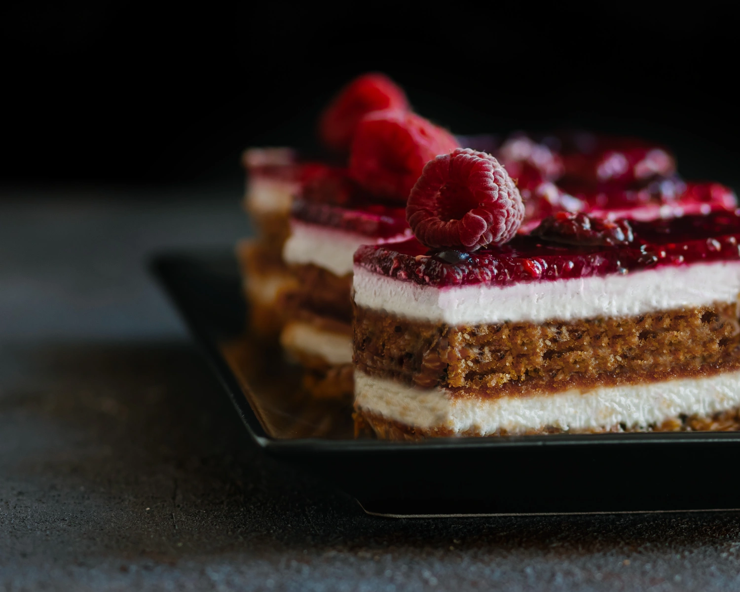 Layered cake slices with brown base, white cream, and red raspberry topping, a sweet homemade gift idea.