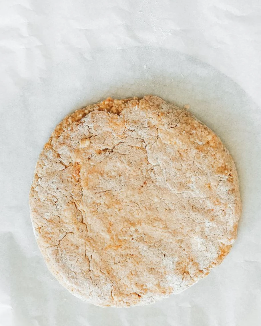 Тиквено тесто за скони, оформено на диск върху хартия за печене, леко набрашнено и готово за рязане по рецептата.