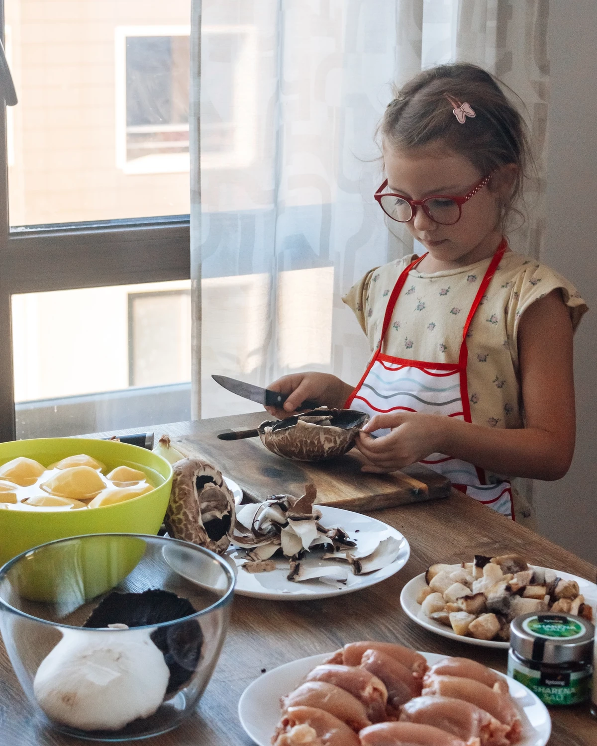 Young girl peeling portobello mushrooms, preparing potato babka (Kugelis) with potatoes, chicken, onions & Sharena Salt.