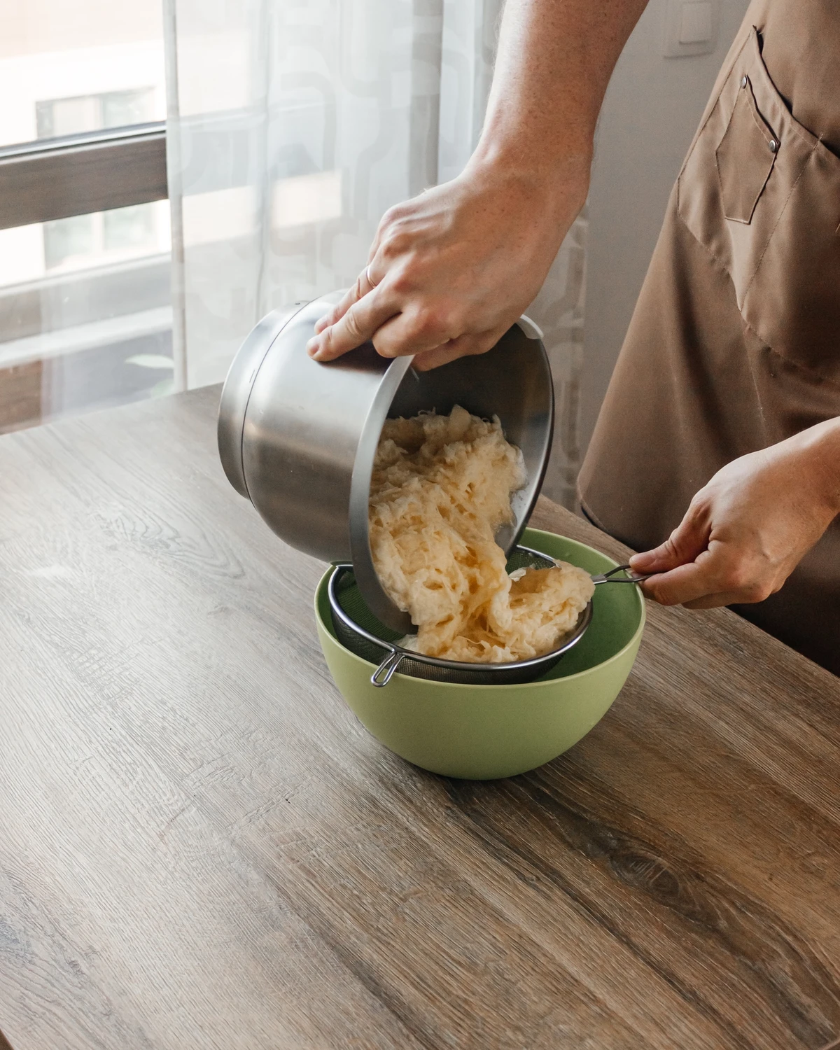 Hands draining grated raw potatoes for Belarusian potato babka or Jewish kugel casserole.