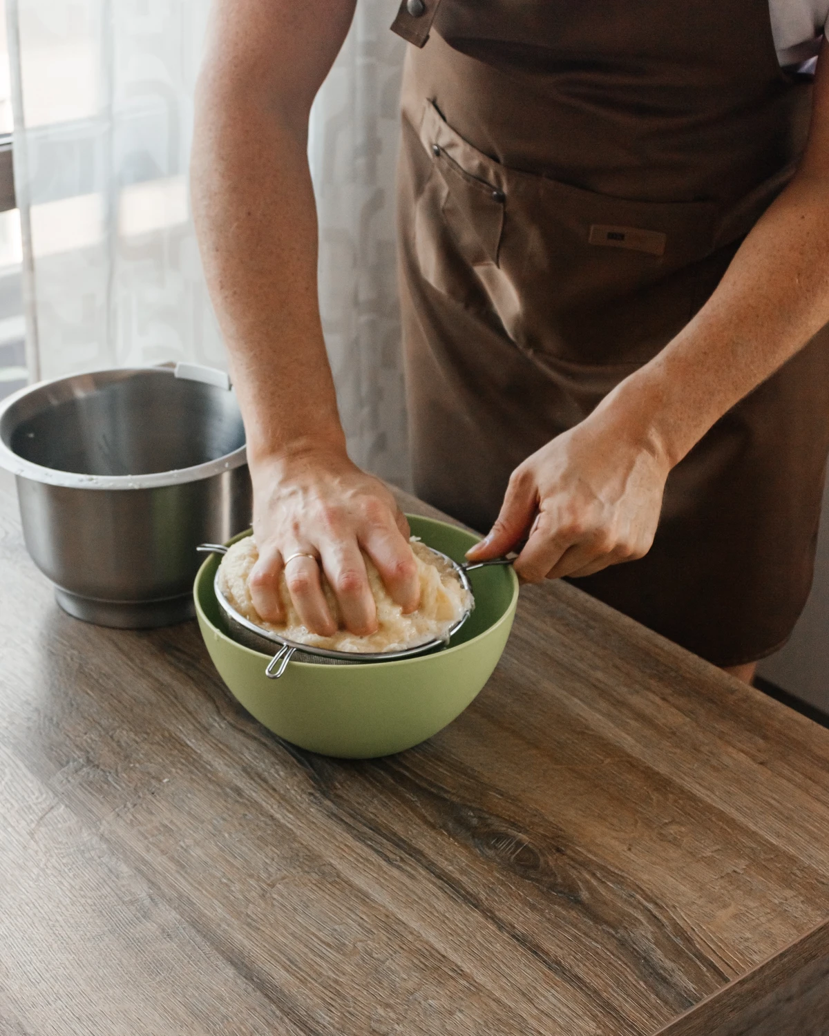 Person pressing grated raw potatoes in a sieve for Belarusian potato babka or kugelis preparation.