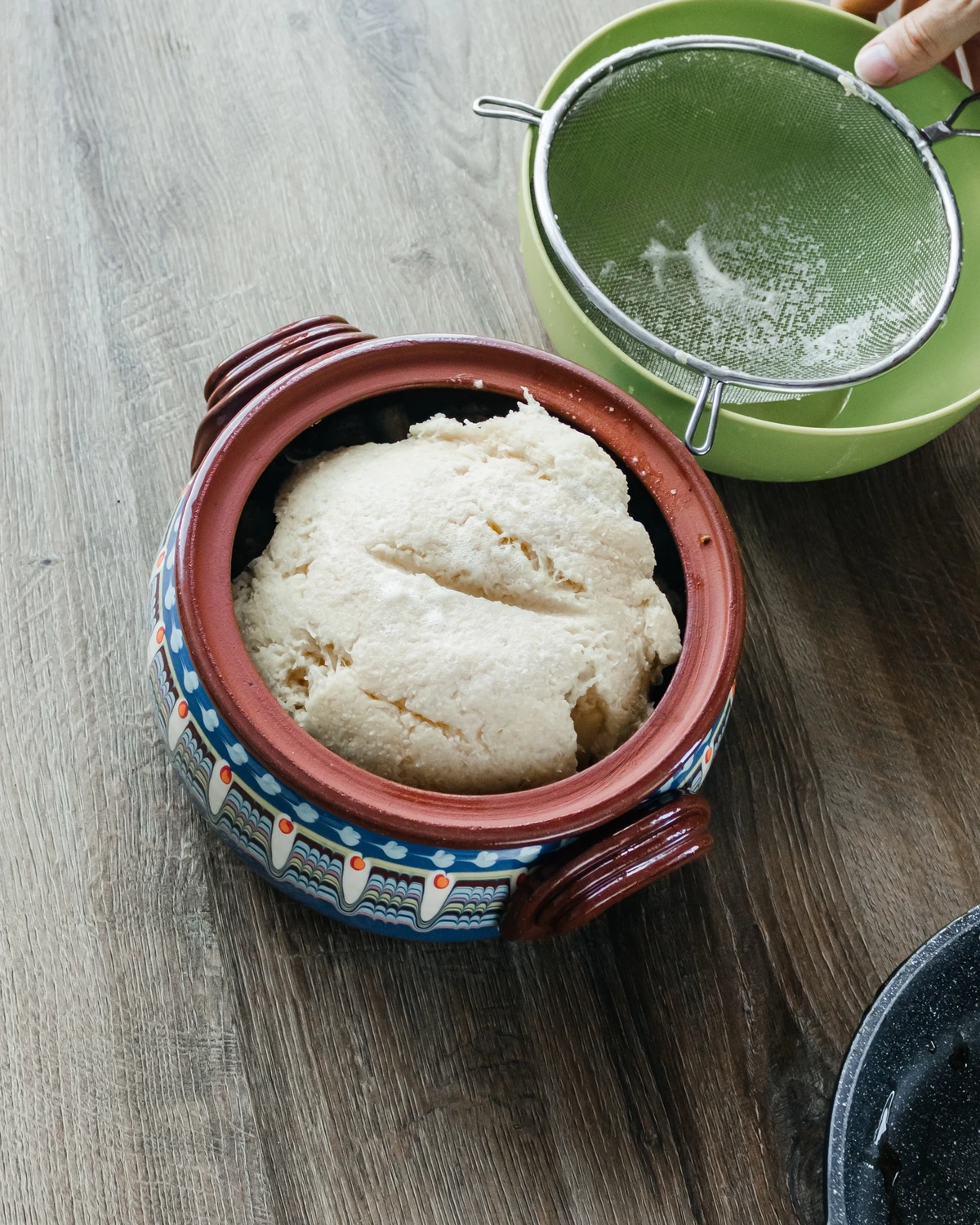 Raw grated potato mixture for babka or kugelis in a decorative clay pot, during preparation.