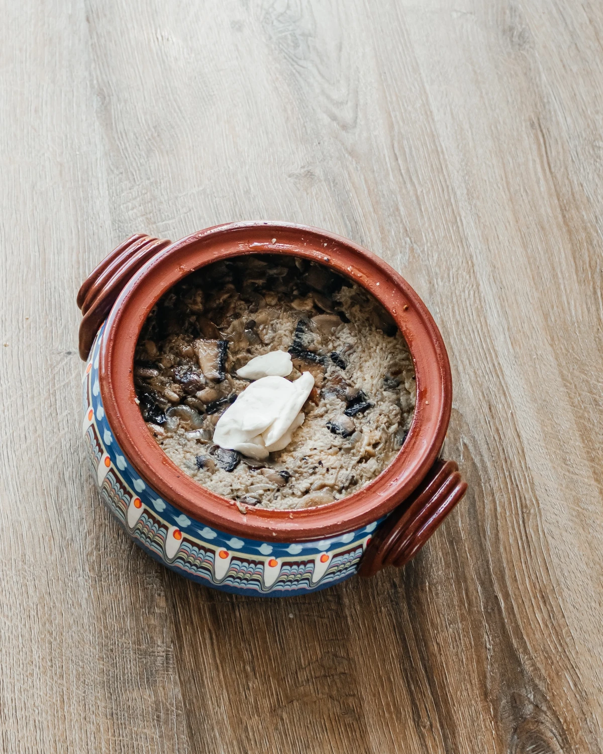 Belarusian potato babka (kugelis) with mushrooms & chicken, topped with cream, in a decorated clay pot.
