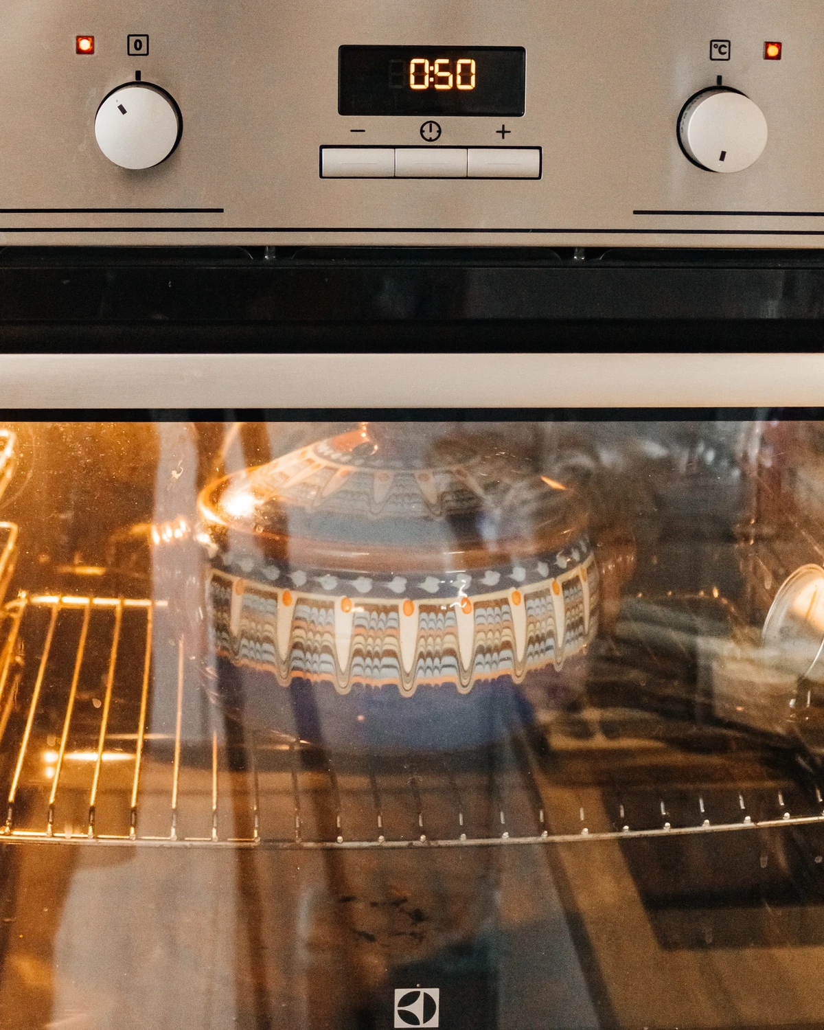 Colorful clay pot with potato babka (kugelis) baking in an Electrolux oven, timer set to 0:50.