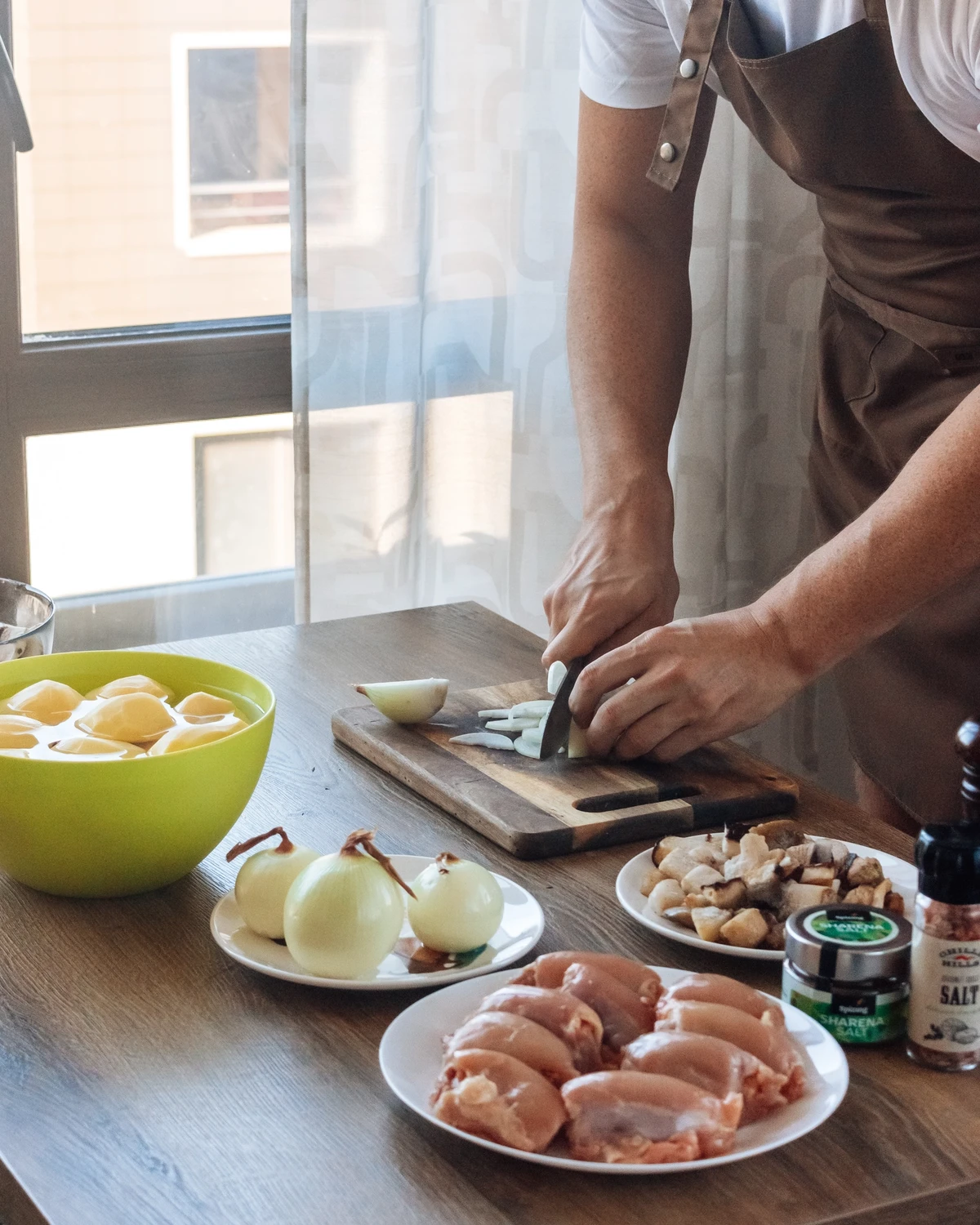 Chef chops onions for potato babka (kugelis), with peeled potatoes, raw chicken, and boletus mushrooms.