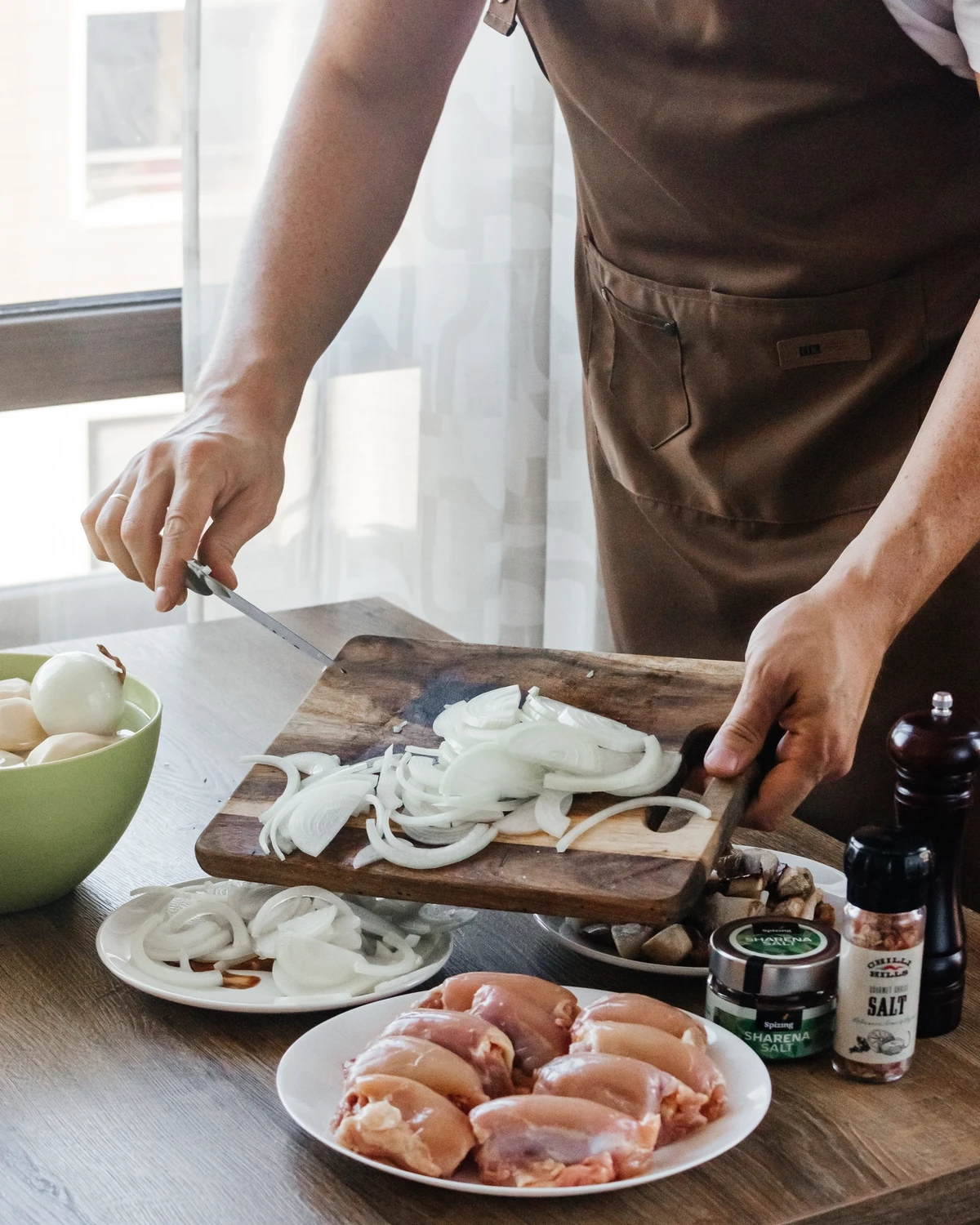 Chef slicing onions for Belarusian potato babka (kugelis). Raw chicken, mushrooms, & Spizing Sharena Salt prep.