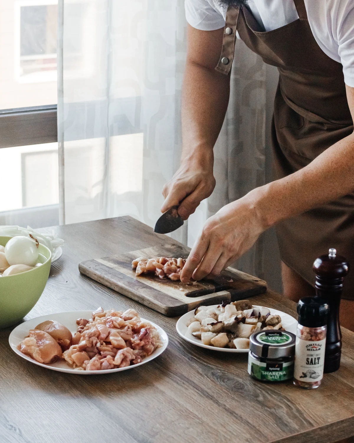 Chef cutting chicken & mushrooms for potato babka (kugelis), with Sharena Salt & spices on a wooden table.