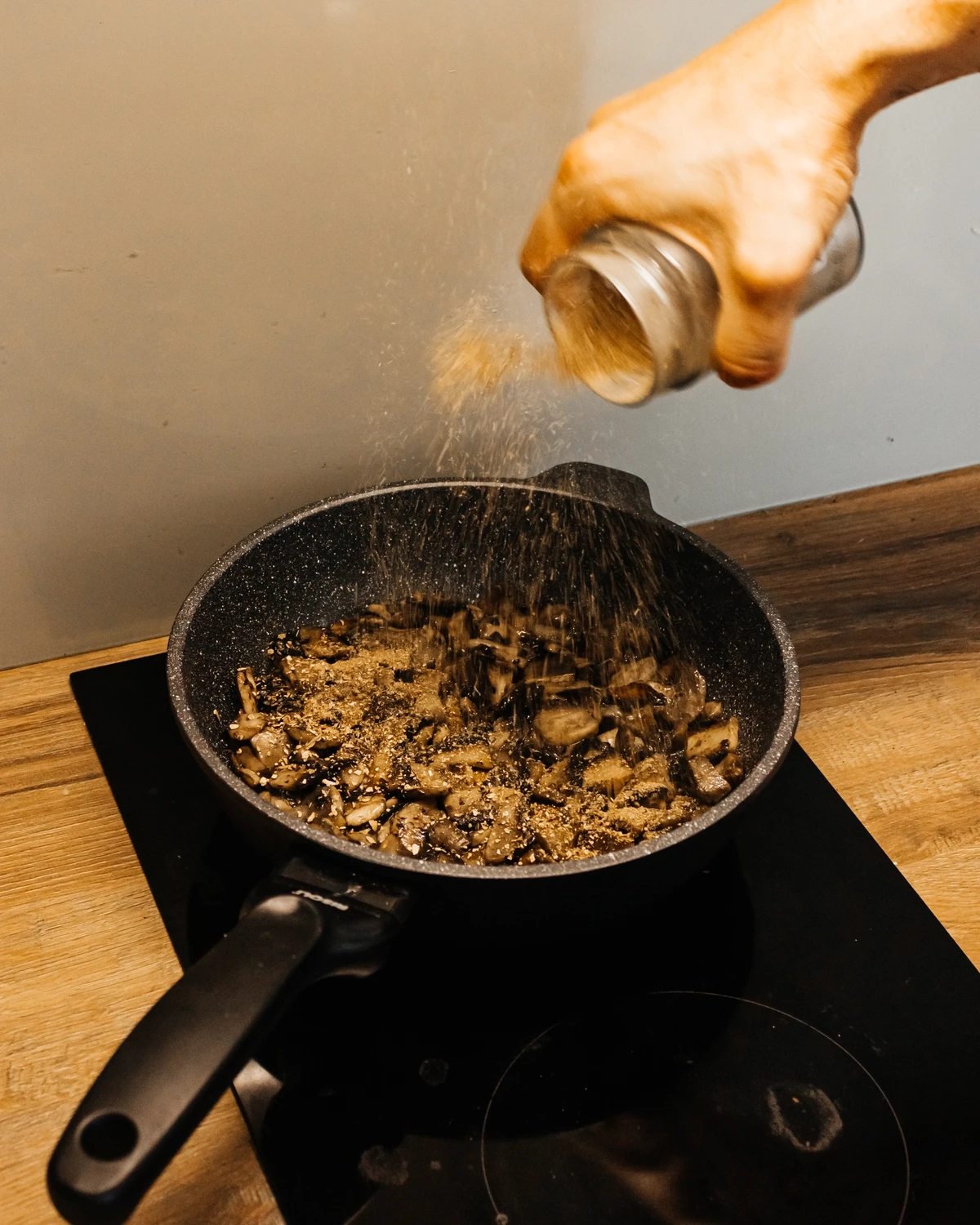 Hand seasoning Portobello mushrooms frying in a pan for Belarusian potato babka or Jewish kugel.