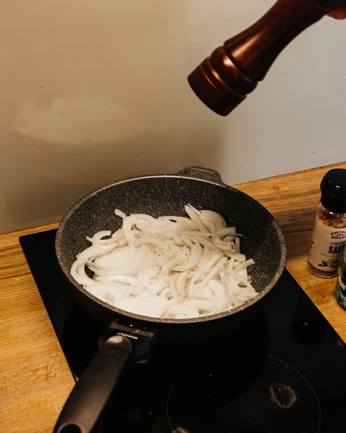 Sliced onions being seasoned in a pan on a cooktop, a crucial step for the delicious potato babka/kugelis recipe.