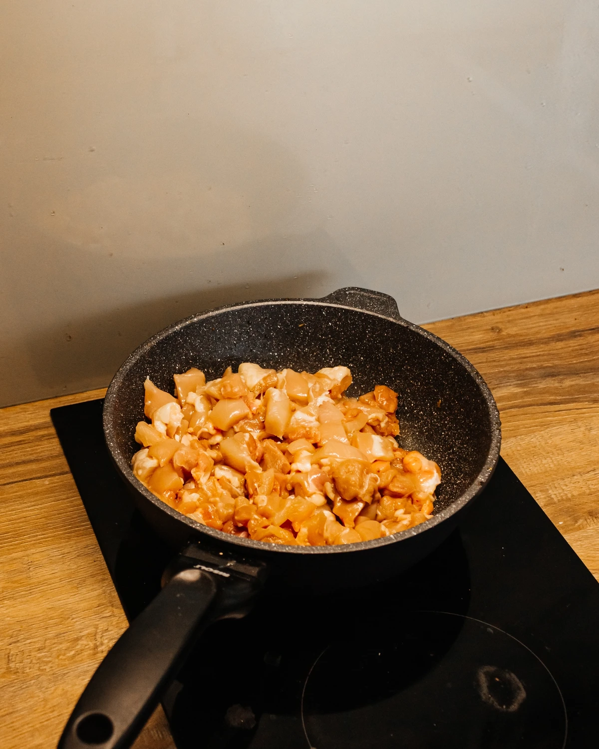 Raw diced chicken in a pan on an induction cooktop, an ingredient for Kugel or potato babka filling.