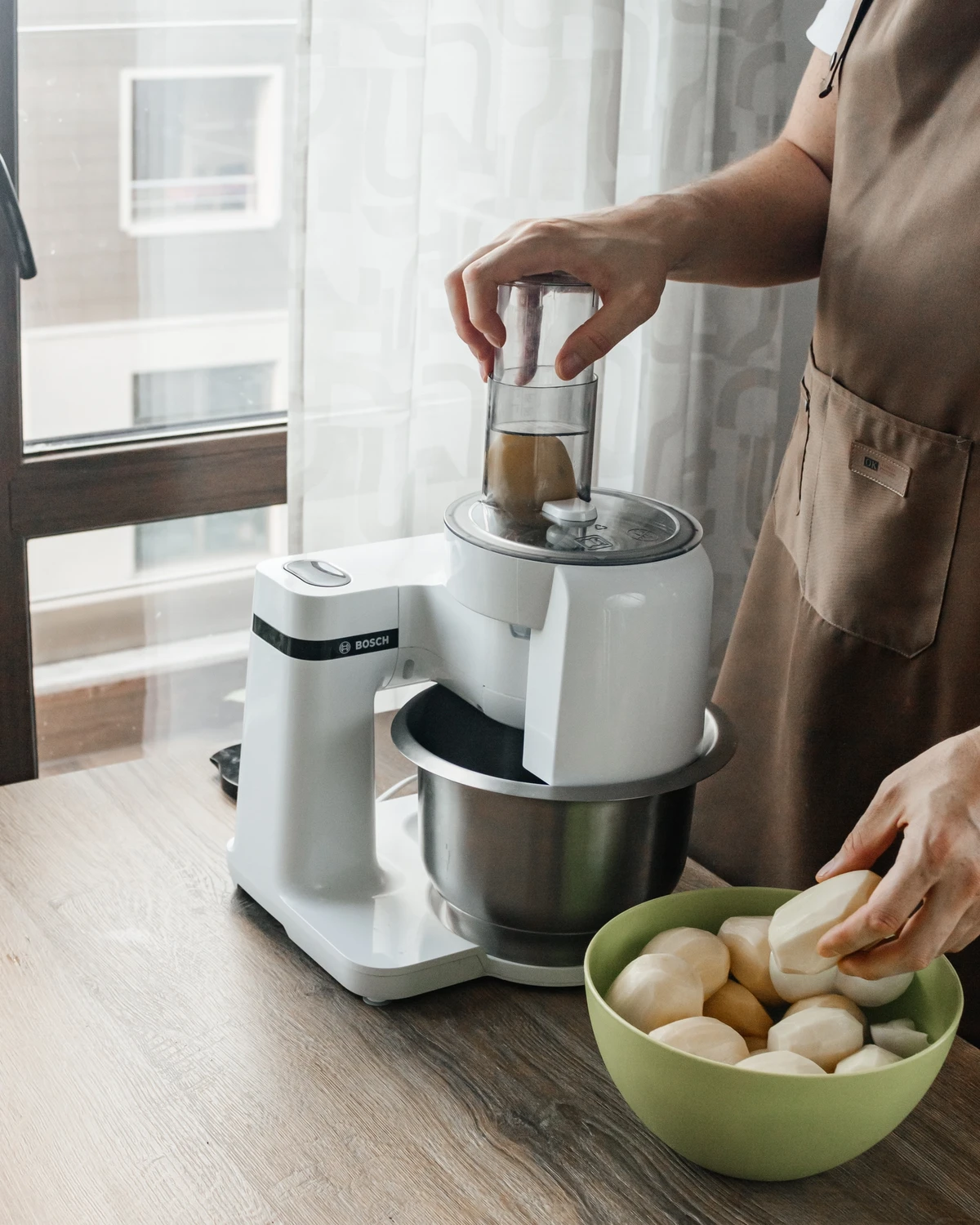 Grating raw potatoes with a Bosch kitchen machine for Kugel or traditional Belarusian potato babka.