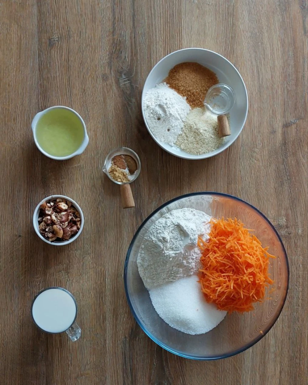 Fresh ingredients for homemade carrot muffins: shredded carrots, flour, sugars, coconut milk, oil, nuts, spices.