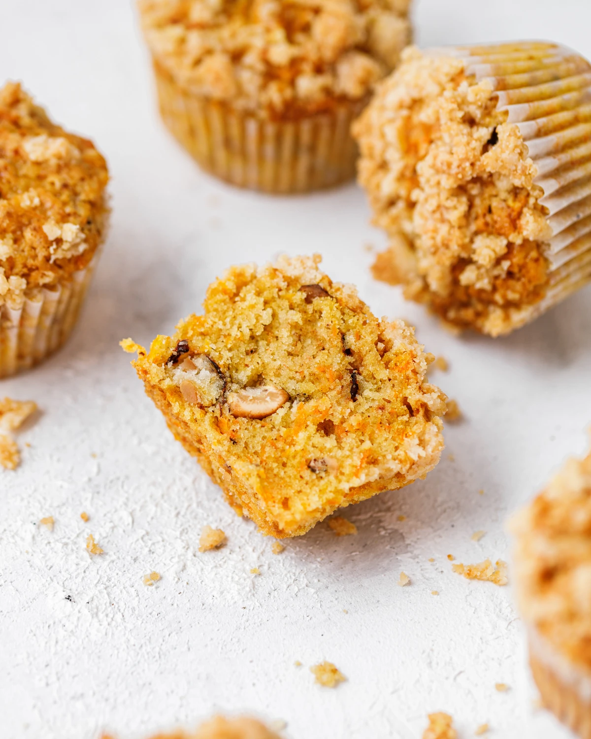 Delicious carrot muffins with crunchy crumble topping; one broken open showing nuts and carrots. Easy recipe.