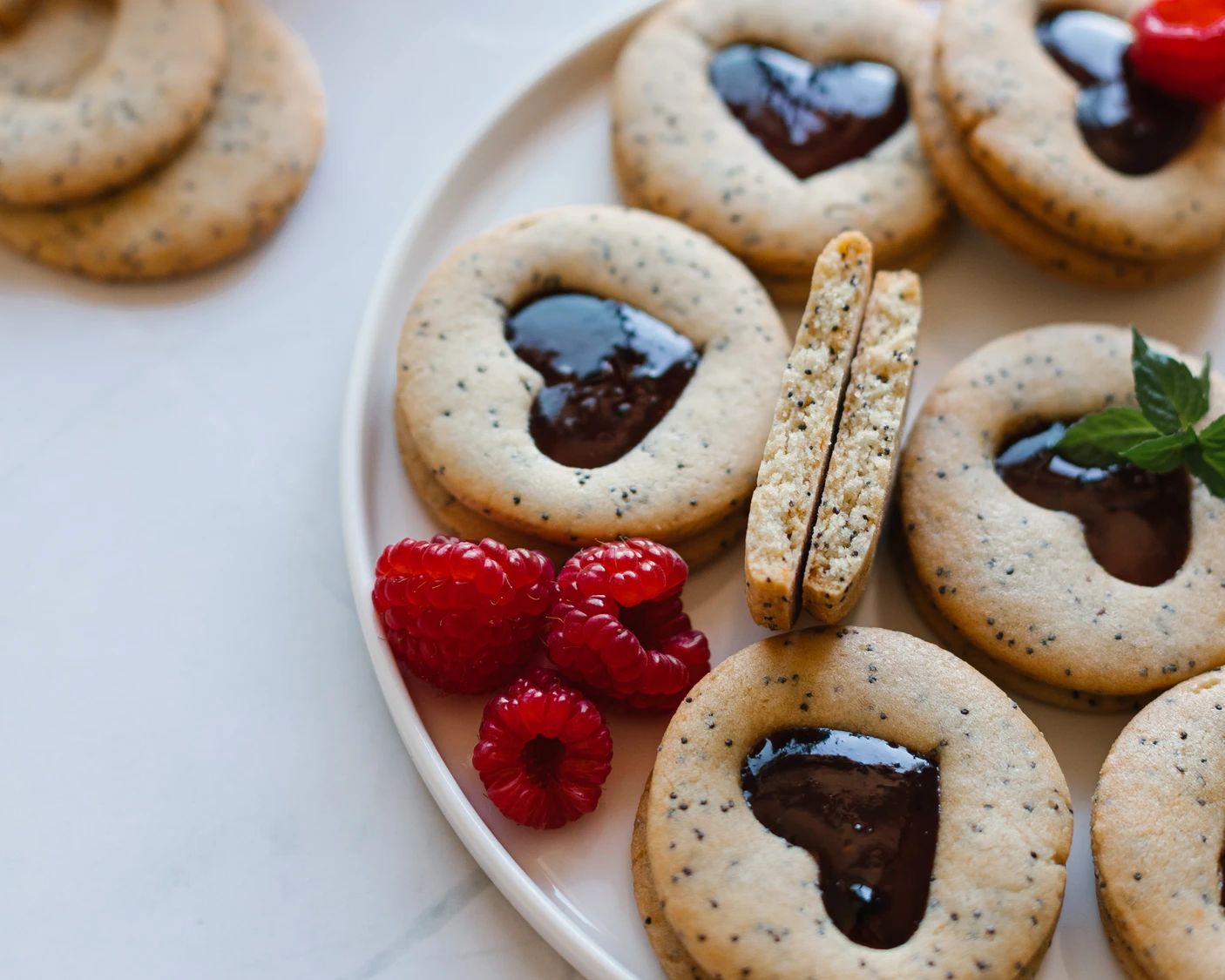 Poppy seed shortbread cookies with heart jam fillings, fresh raspberries, and mint for Mother's Day or afternoon tea.