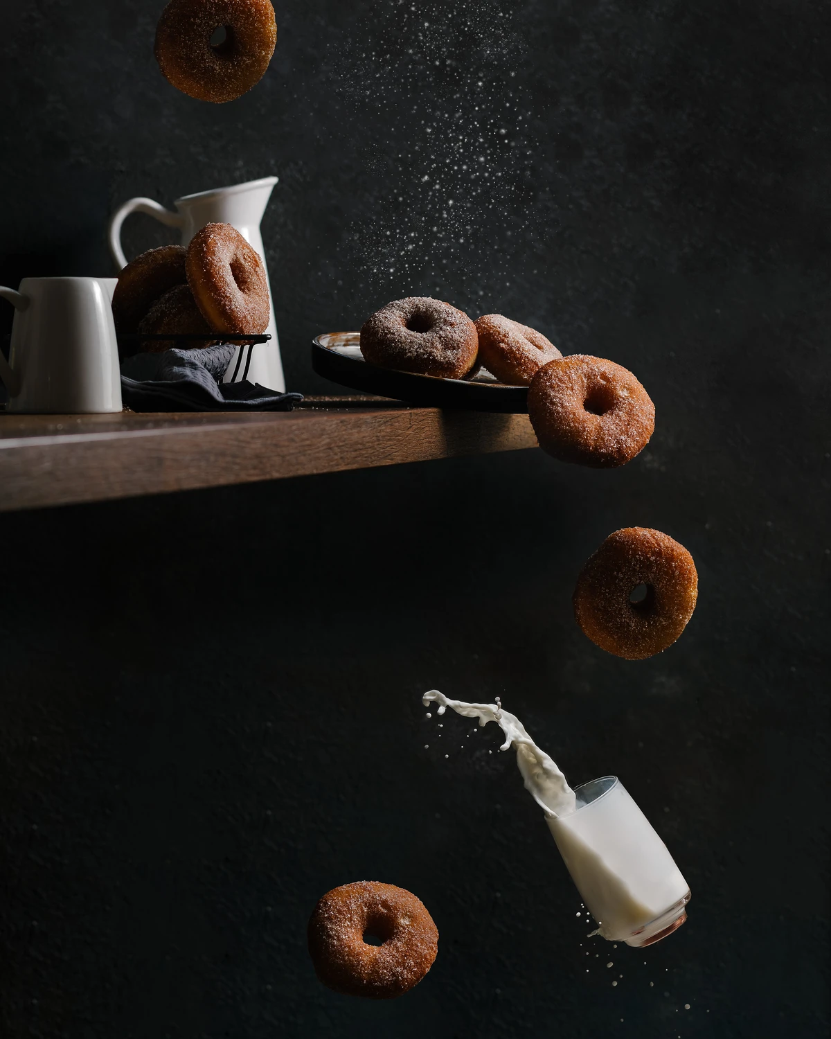 Freshly fried homemade sugar-cinnamon donuts falling with a splashing glass of milk.